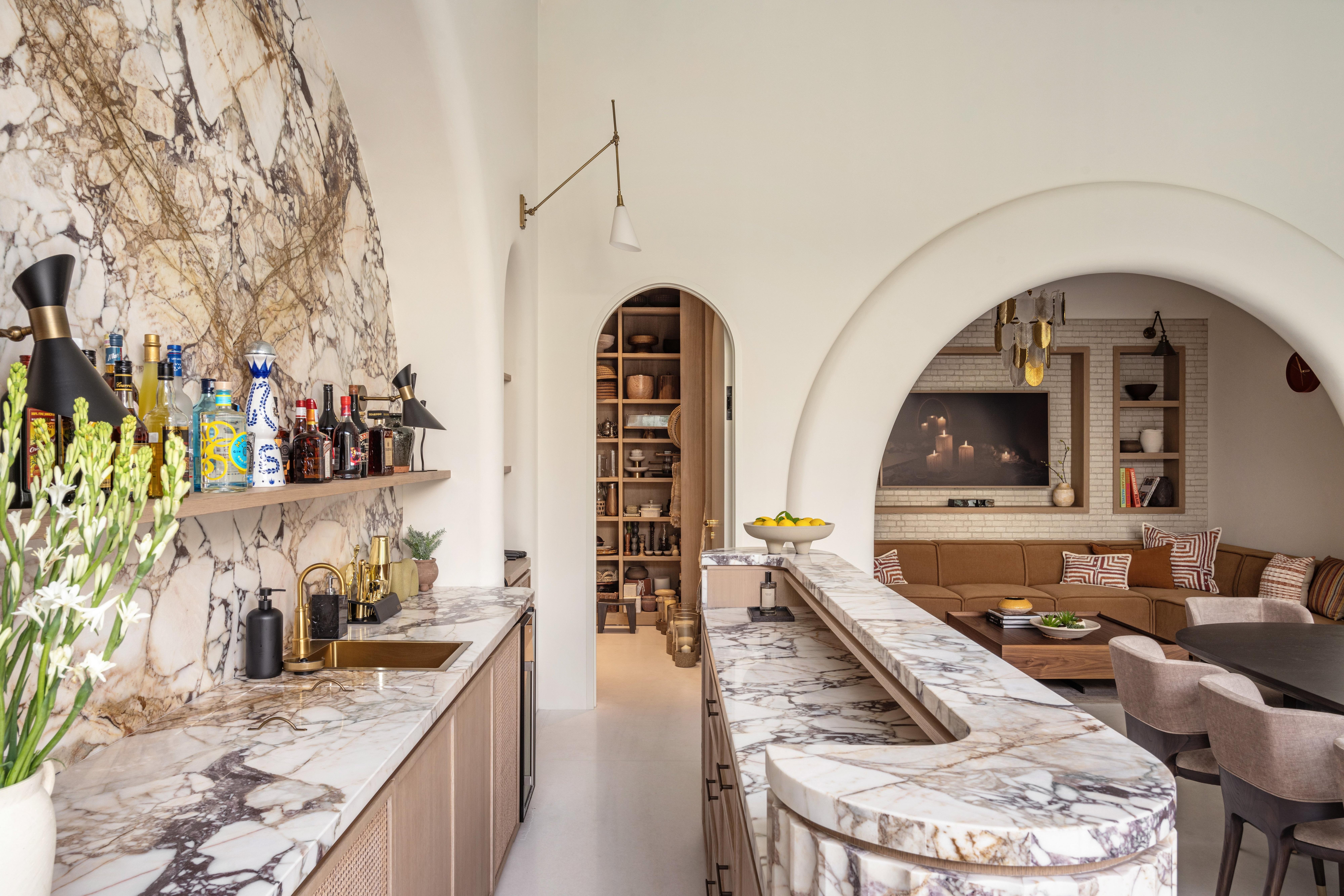 Marble-topped kitchen bar with sink, drinks shelf and stools, opening into a lounge area.