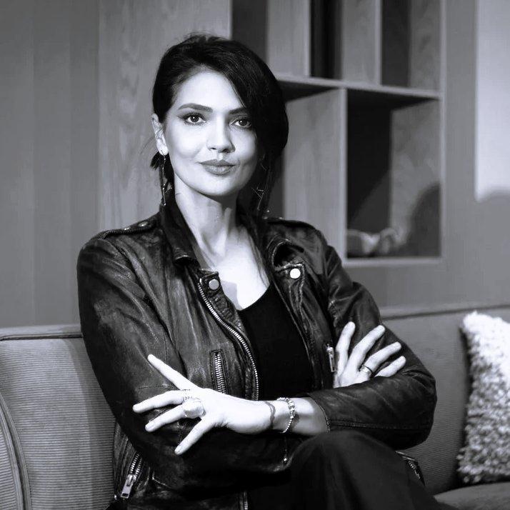 Woman wearing a leather jacket sitting on a sofa with arms crossed.