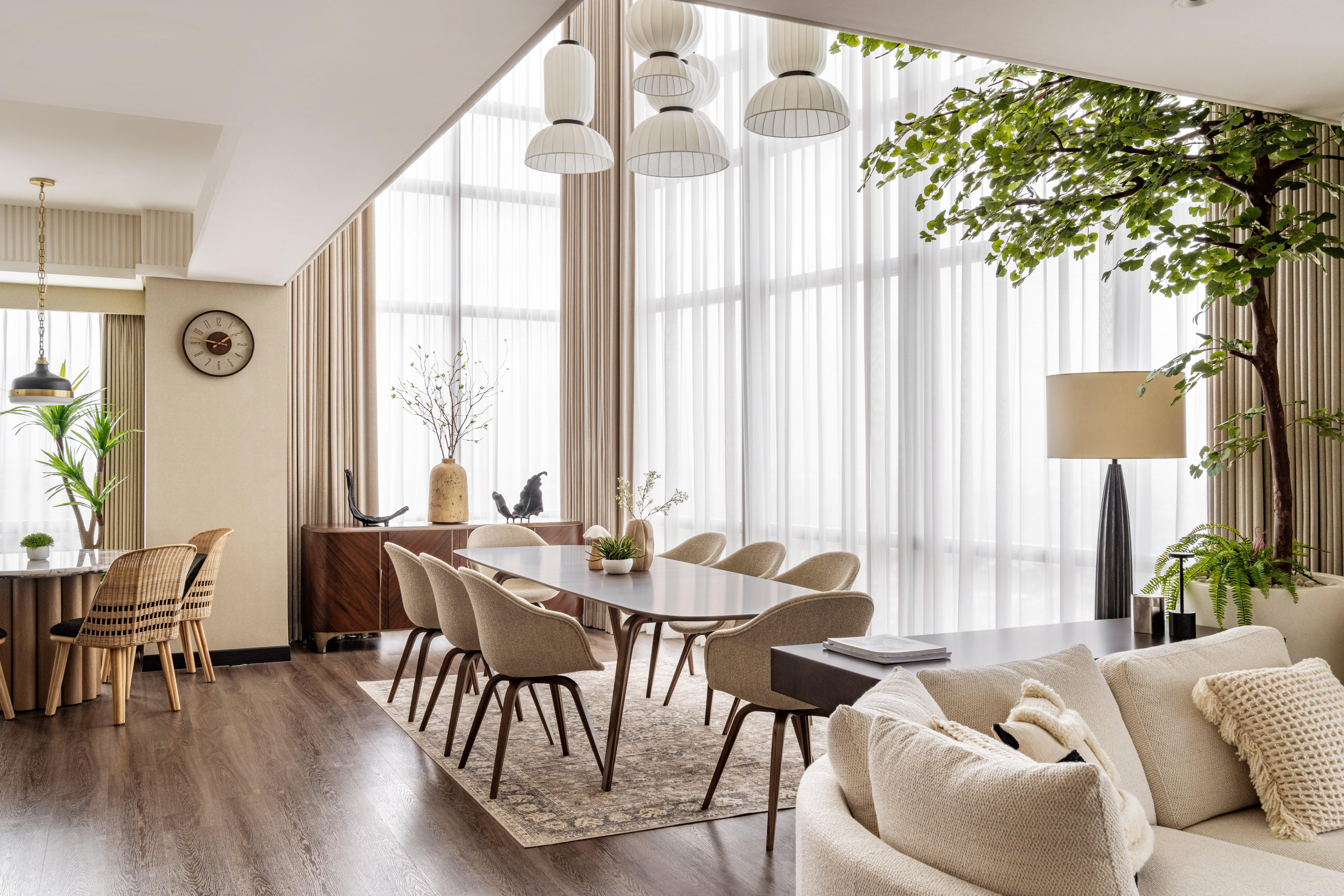Modern dining room with long table, upholstered chairs and pendant lights by floor-to-ceiling windows.