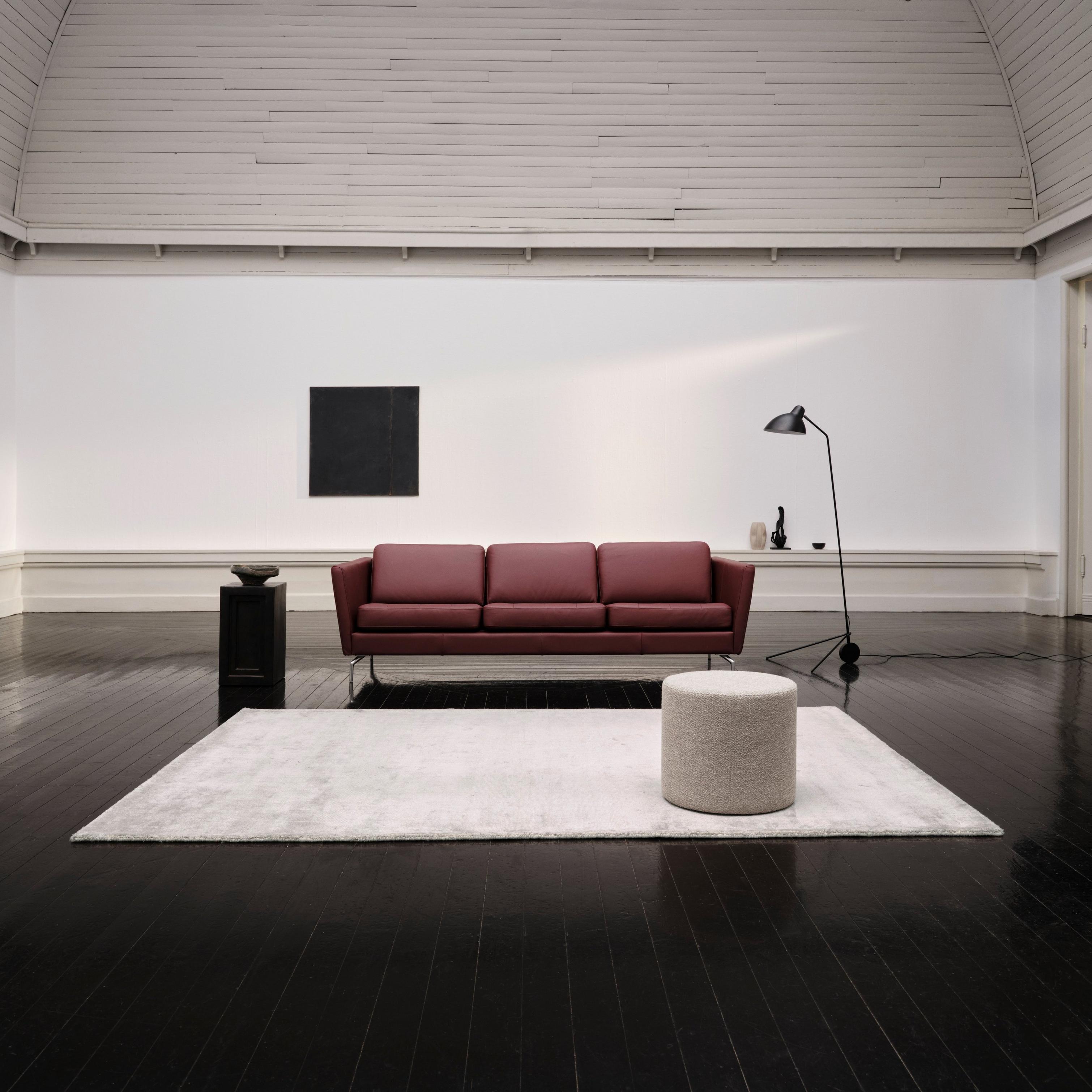 Modern living room with a red sofa, black floor lamp, and round ottoman on a light rug.