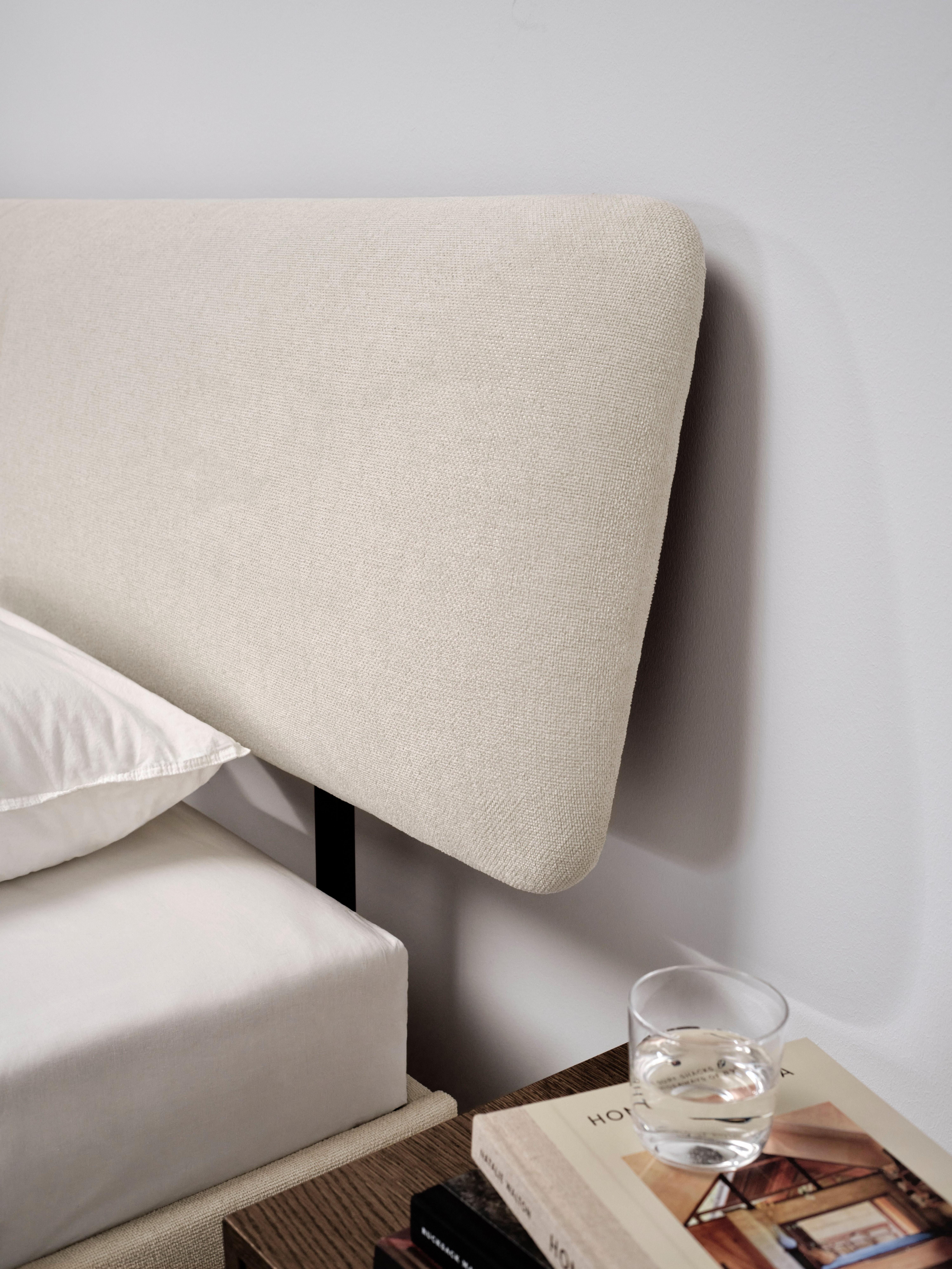 Beige upholstered headboard, white pillow, and books next to a glass of water on a bedside table.