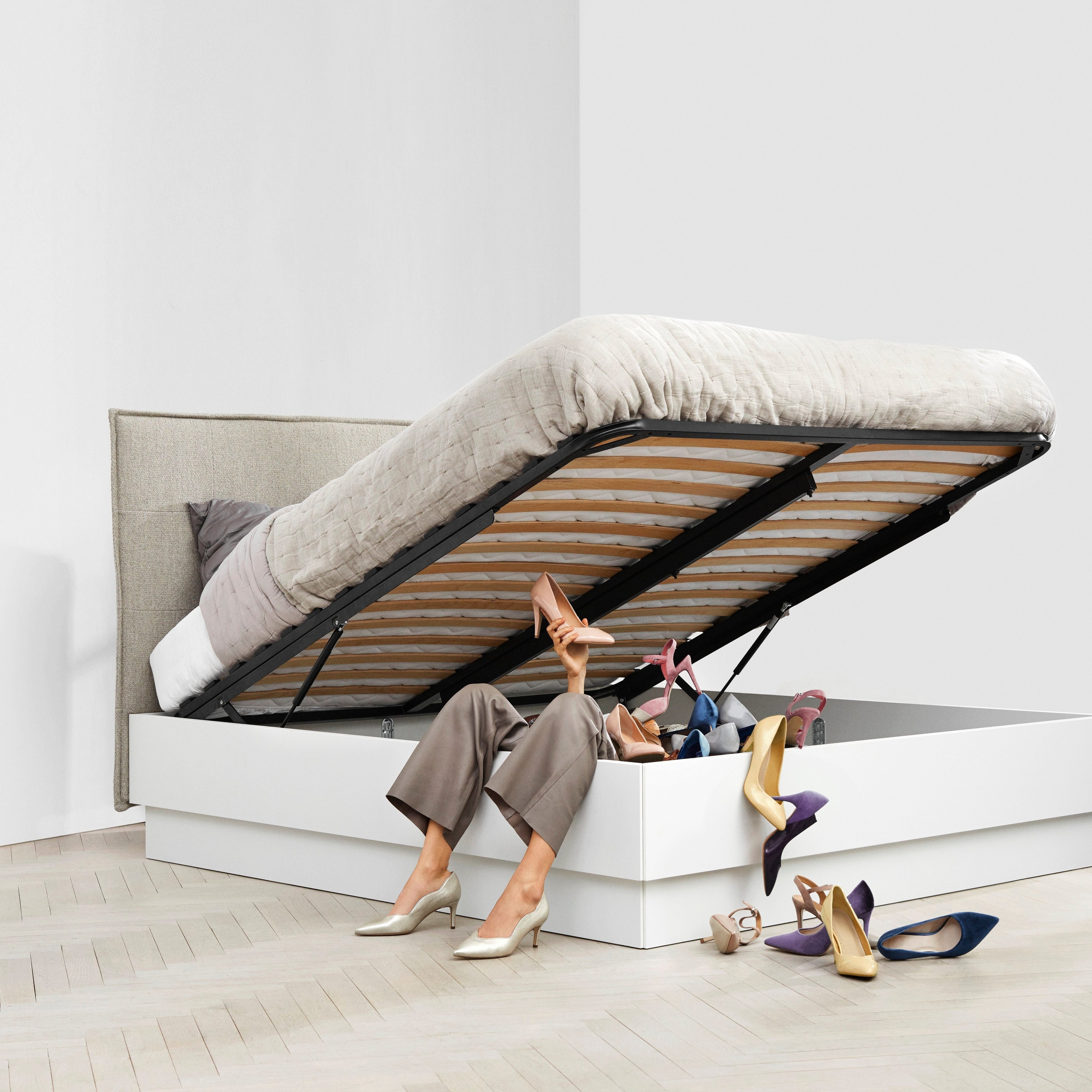 Женщина сидит под поднятой кроватью с пространством для хранения в окружении разбросанных туфель.
