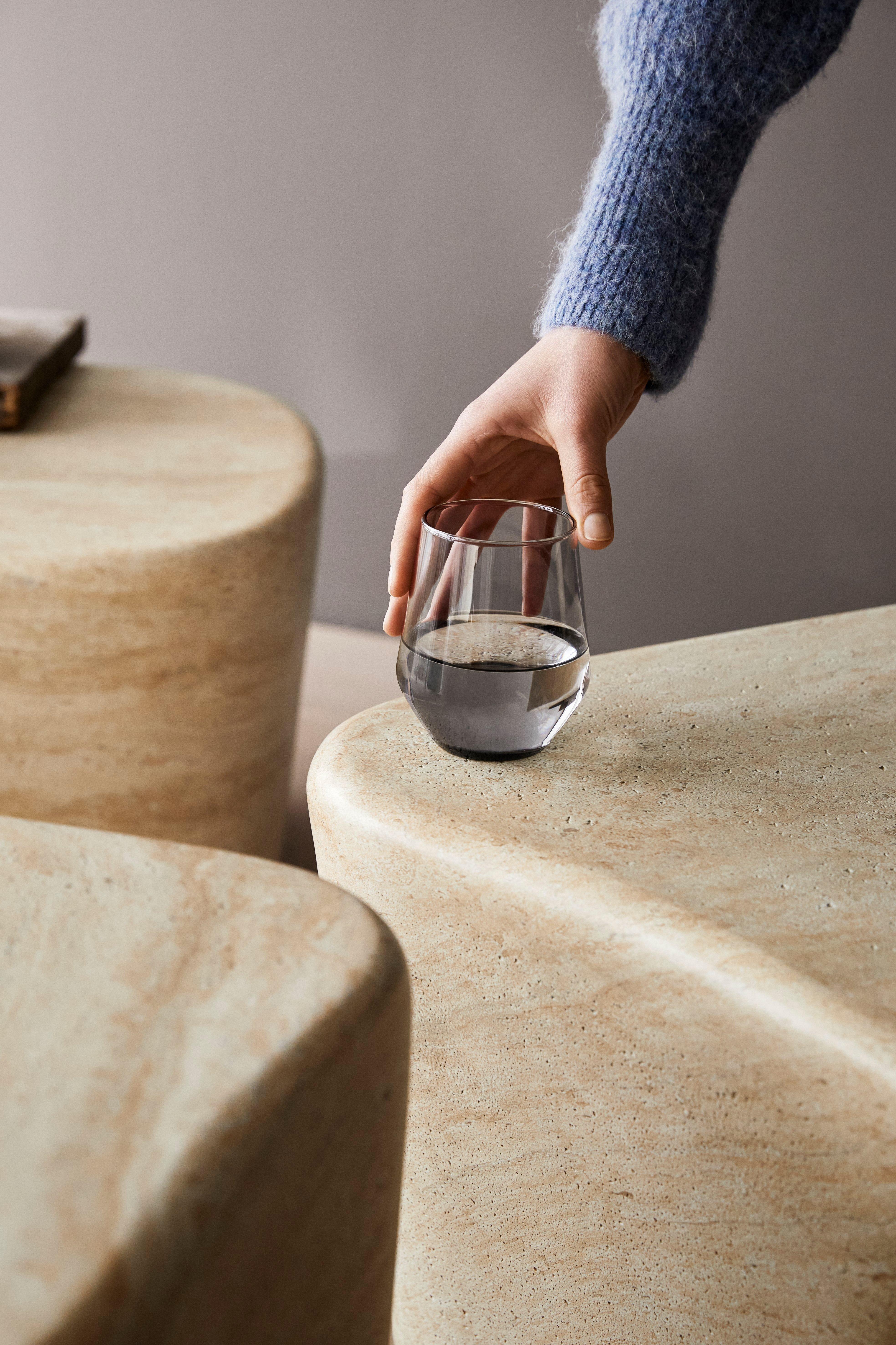 Mano colocando un vaso de agua sobre una mesa de centro Terracina lisa.