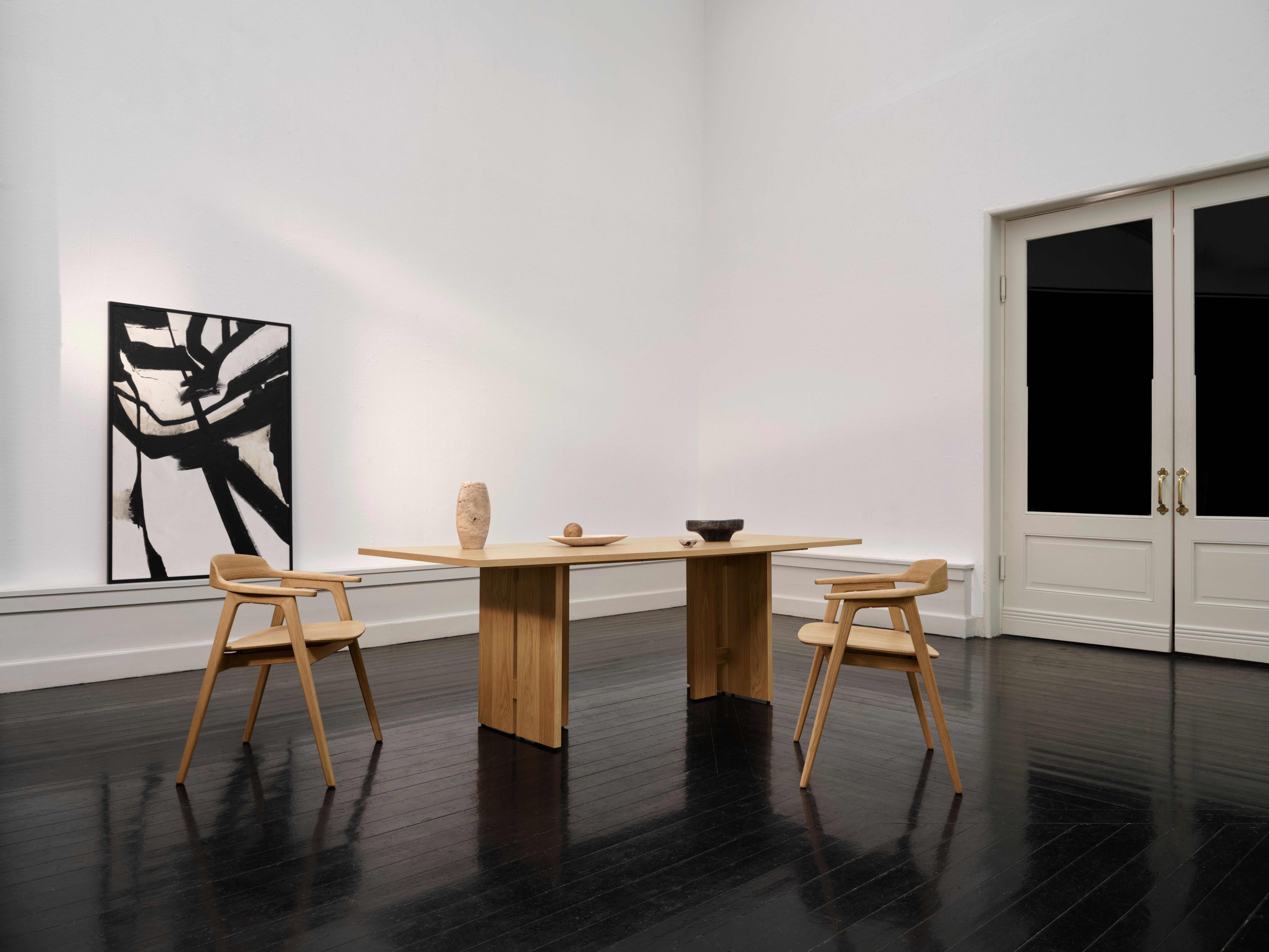 Holztisch mit zwei Stühlen, Keramikvase und Schale. Abstraktes Gemälde an der Wand.