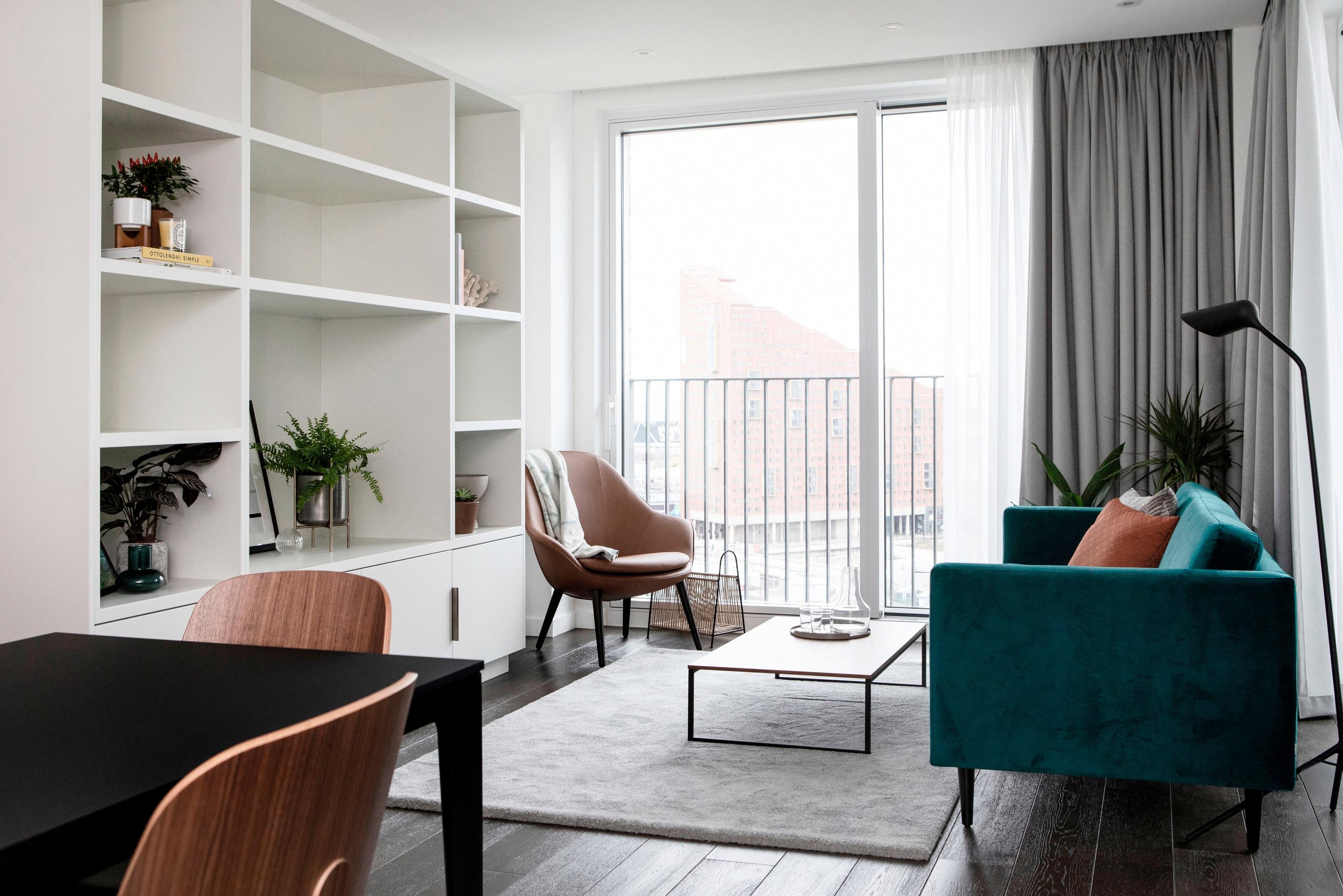 Bright room with bookshelf, chairs, and balcony access, with city view.