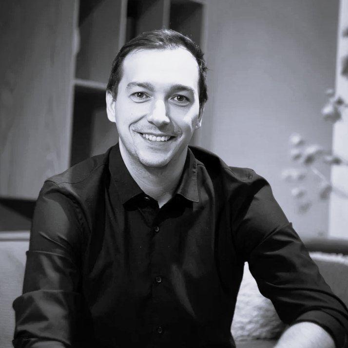 Smiling man in a black button-up shirt sitting indoors.