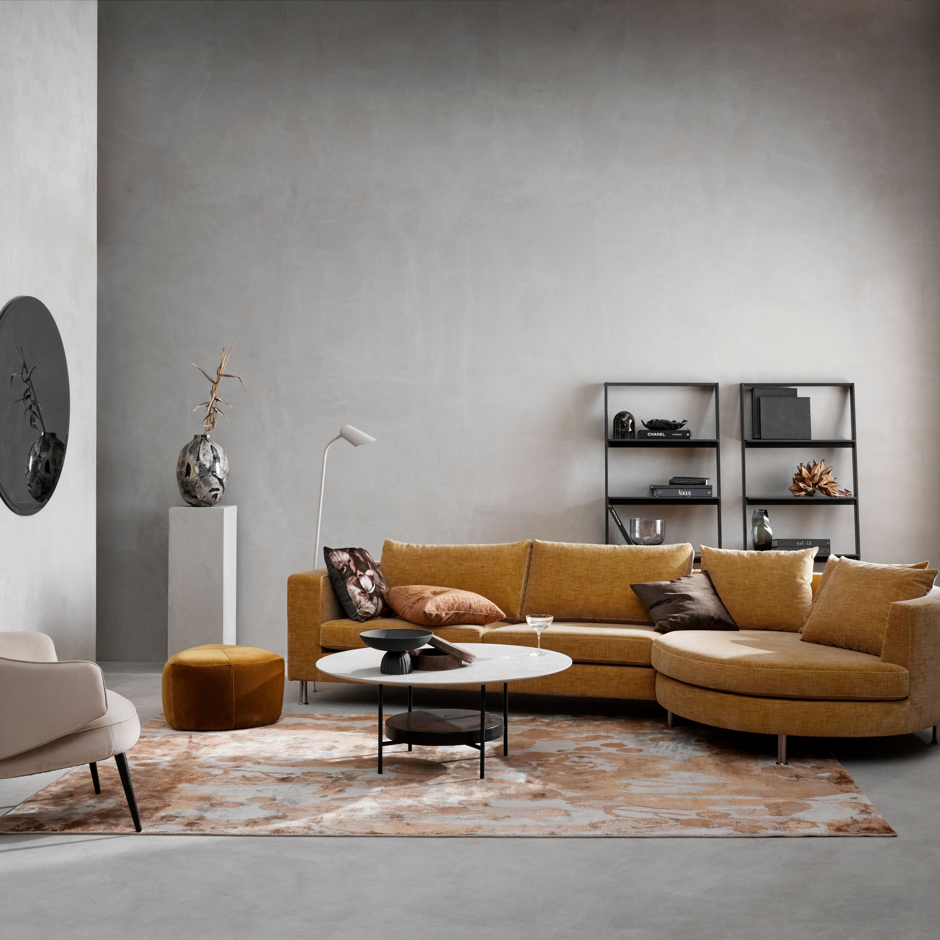 Modernt vardagsrum med senapsfärgad modulsoffa, beige stol, mönstrad matta och minimalistisk inredning.