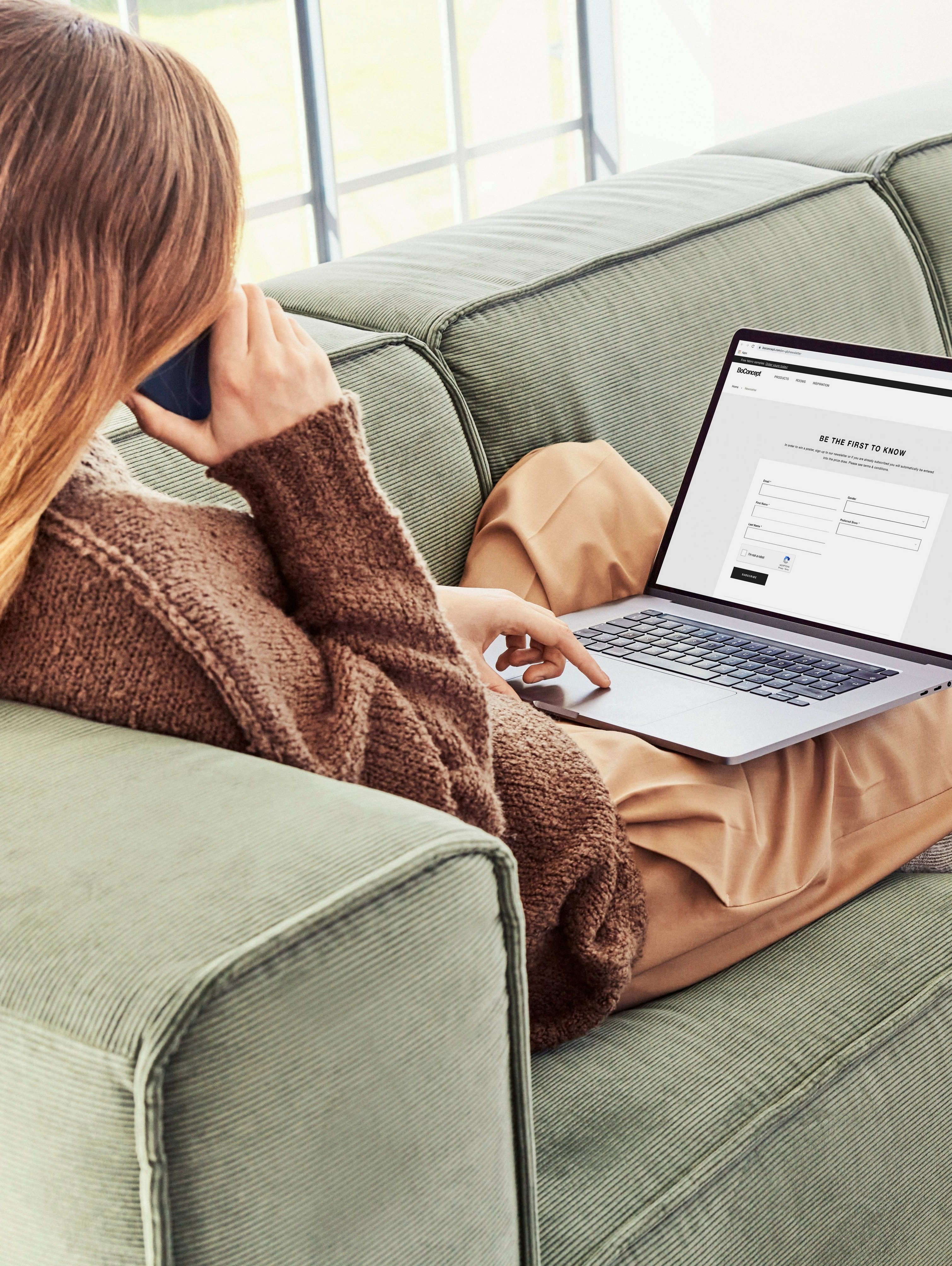 Woman on Carmo green sofa using laptop, with brown clothes and wooden side table.