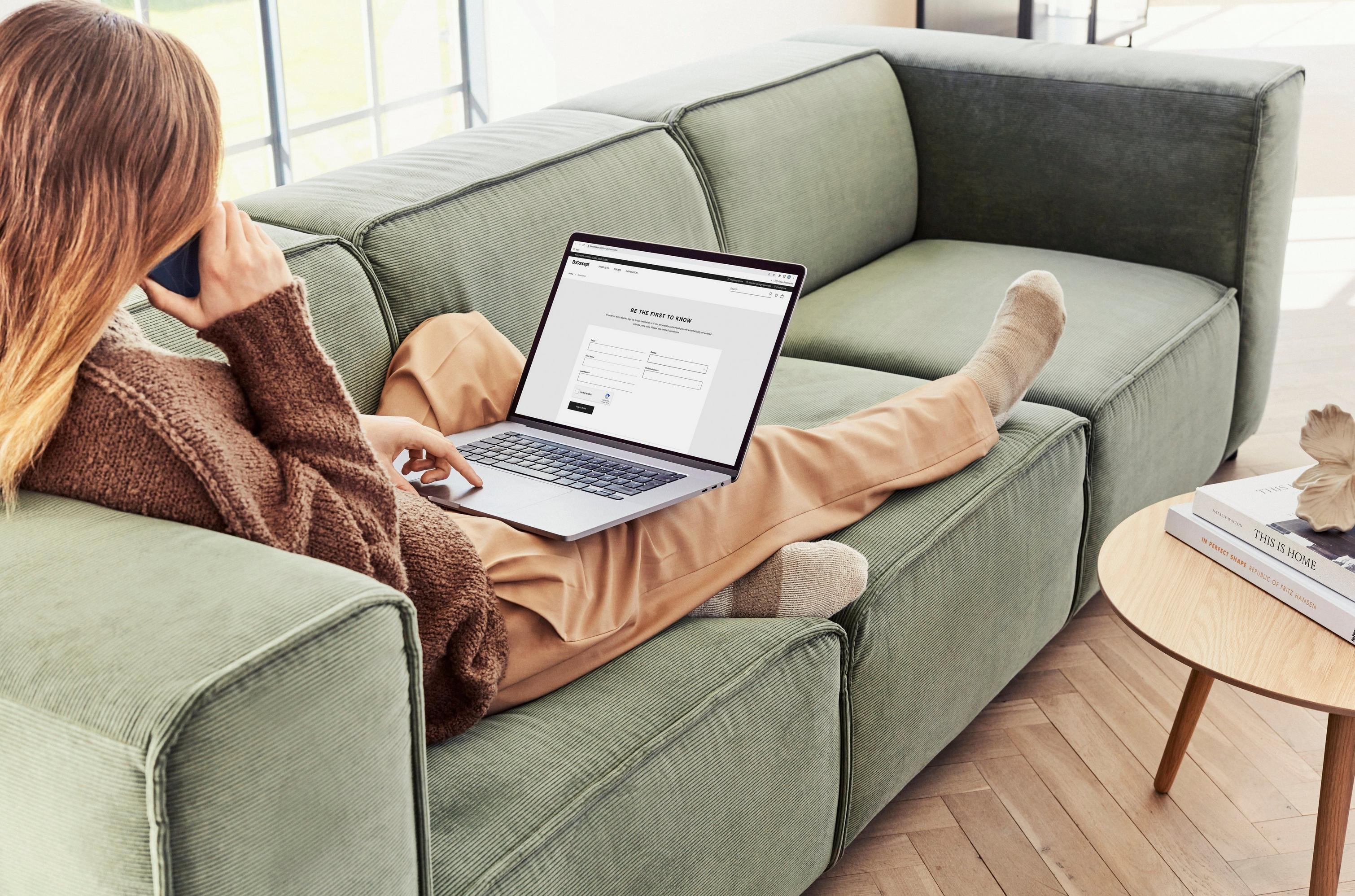 Woman on Carmo green sofa using laptop, with brown clothes and wooden side table.