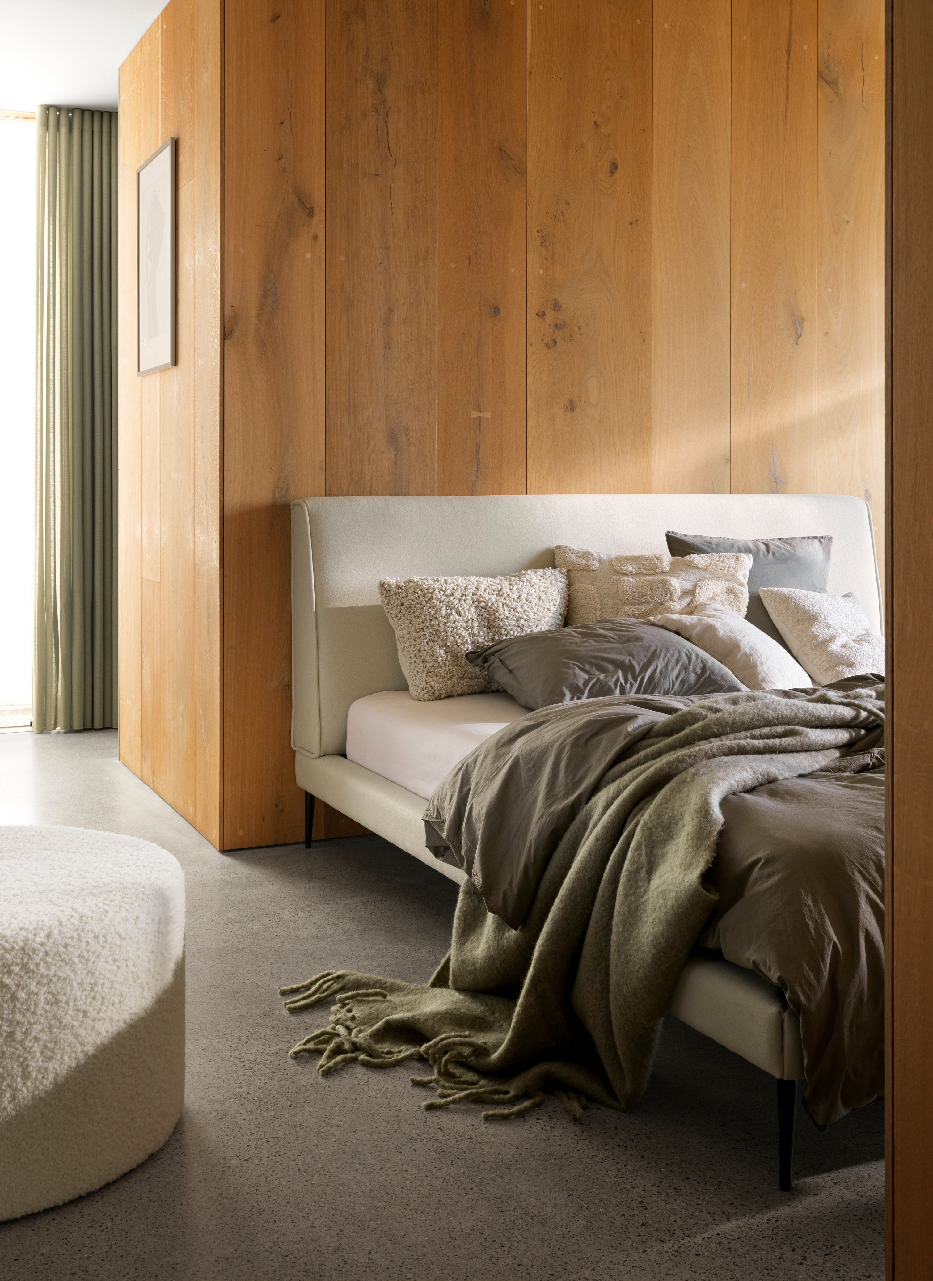 Gezellig bed met zachte plaids en kussens tegen een houten muur en zachte verlichting.