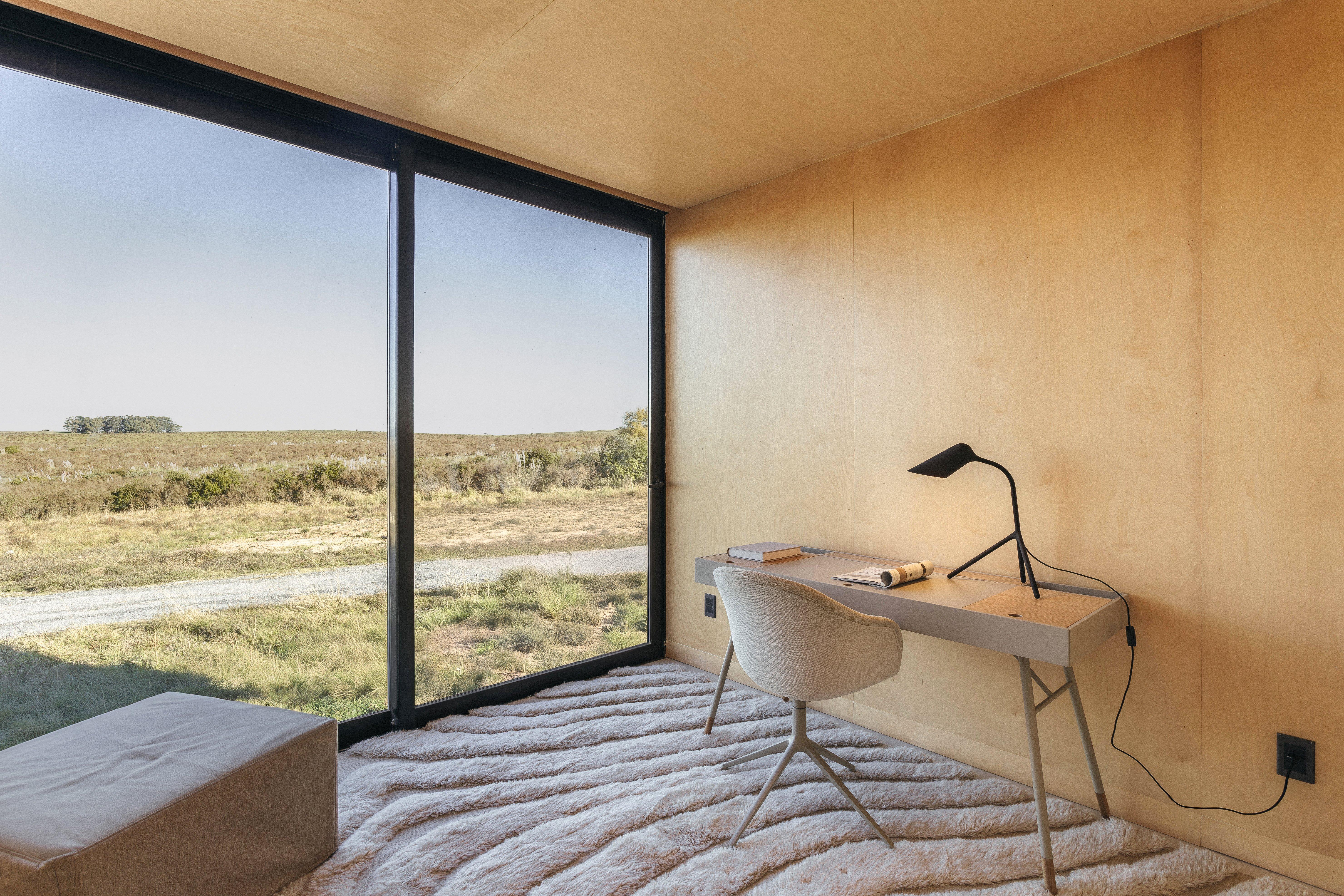 現代化工作室內有桌椅和檯燈，大窗戶外是草原景色。