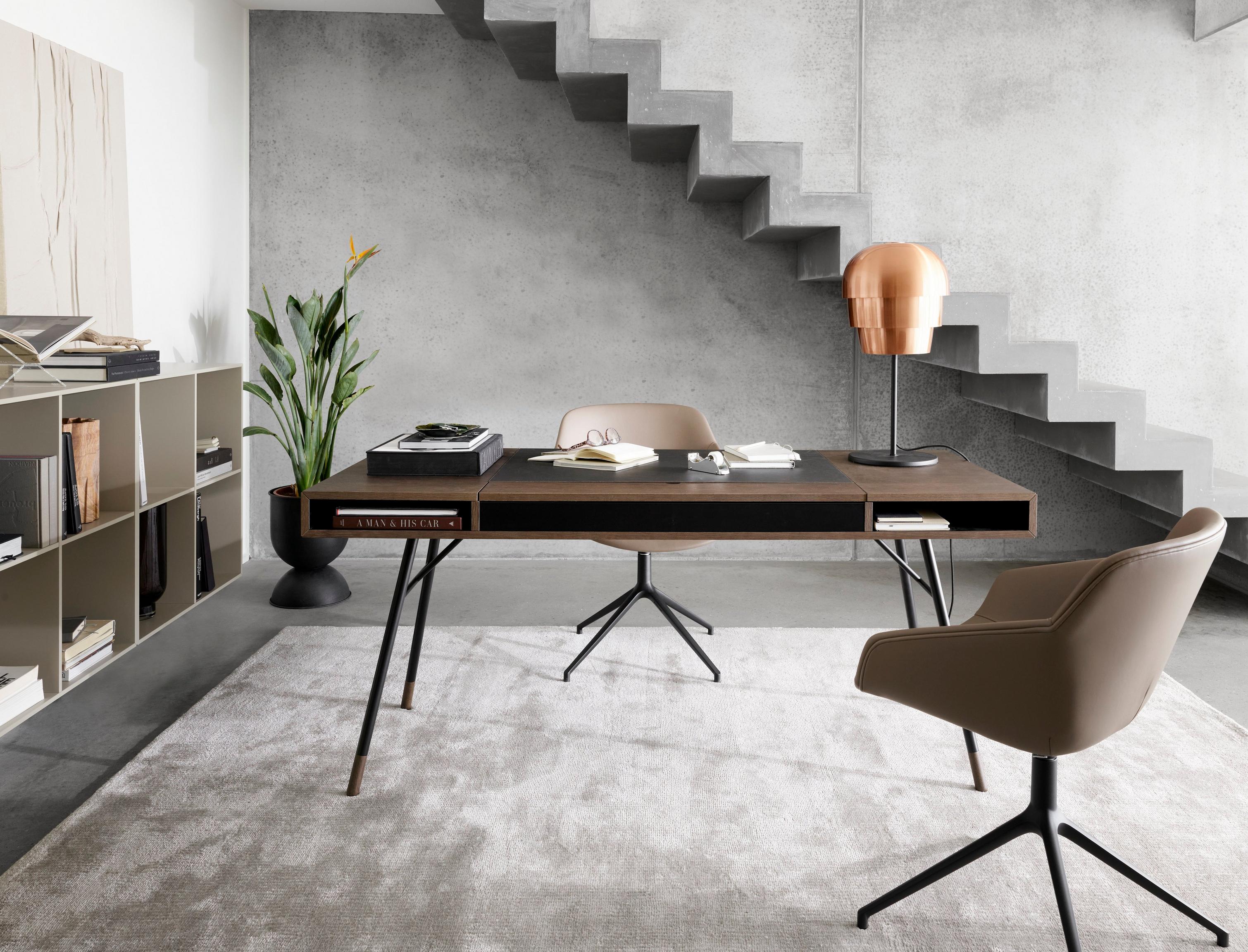 Stylish home office with a dark wood desk, tan chair, and copper lamp near concrete stairs.