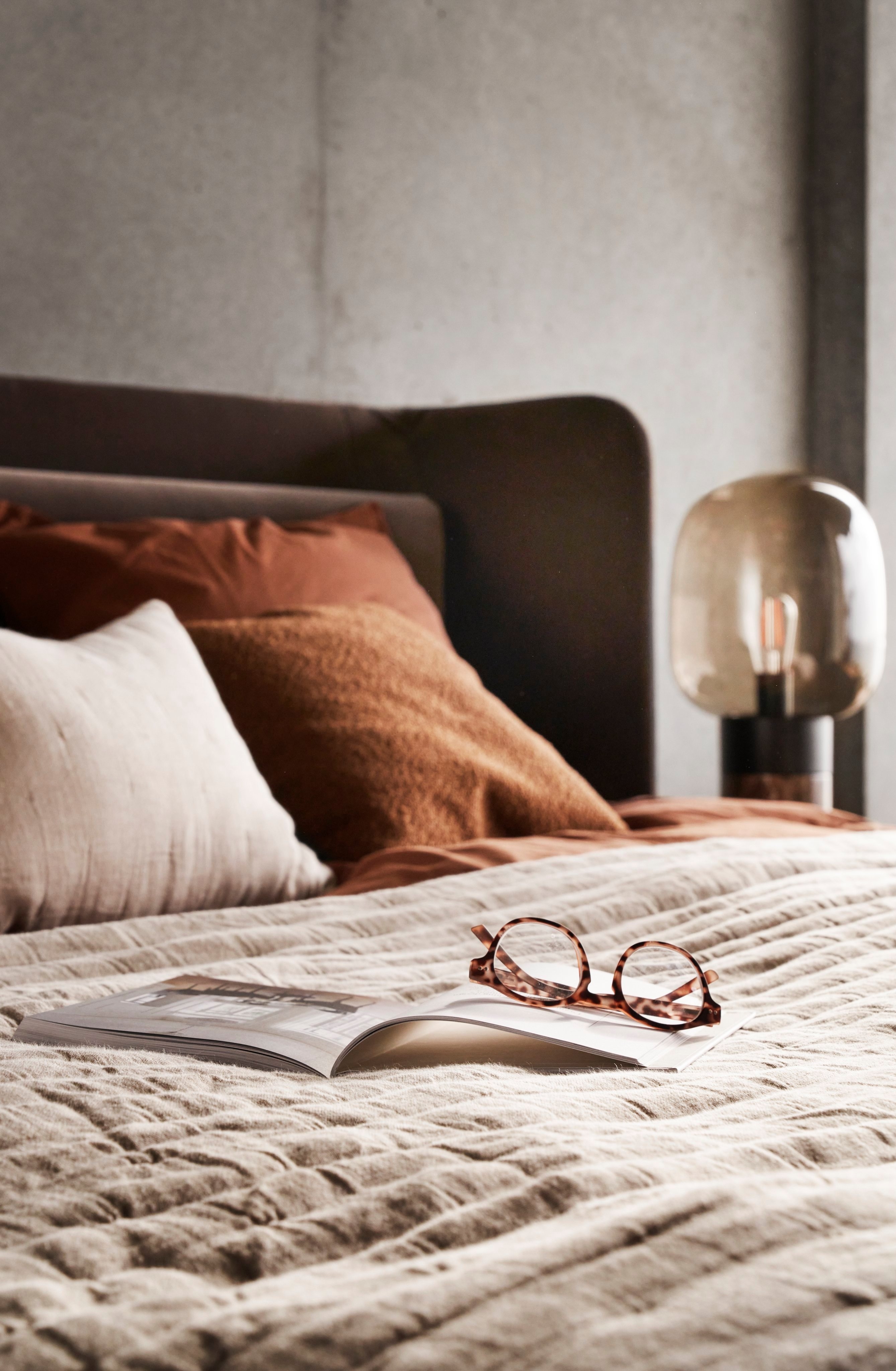 Bed with textured linens, glasses on open book, and soft bedside lighting.