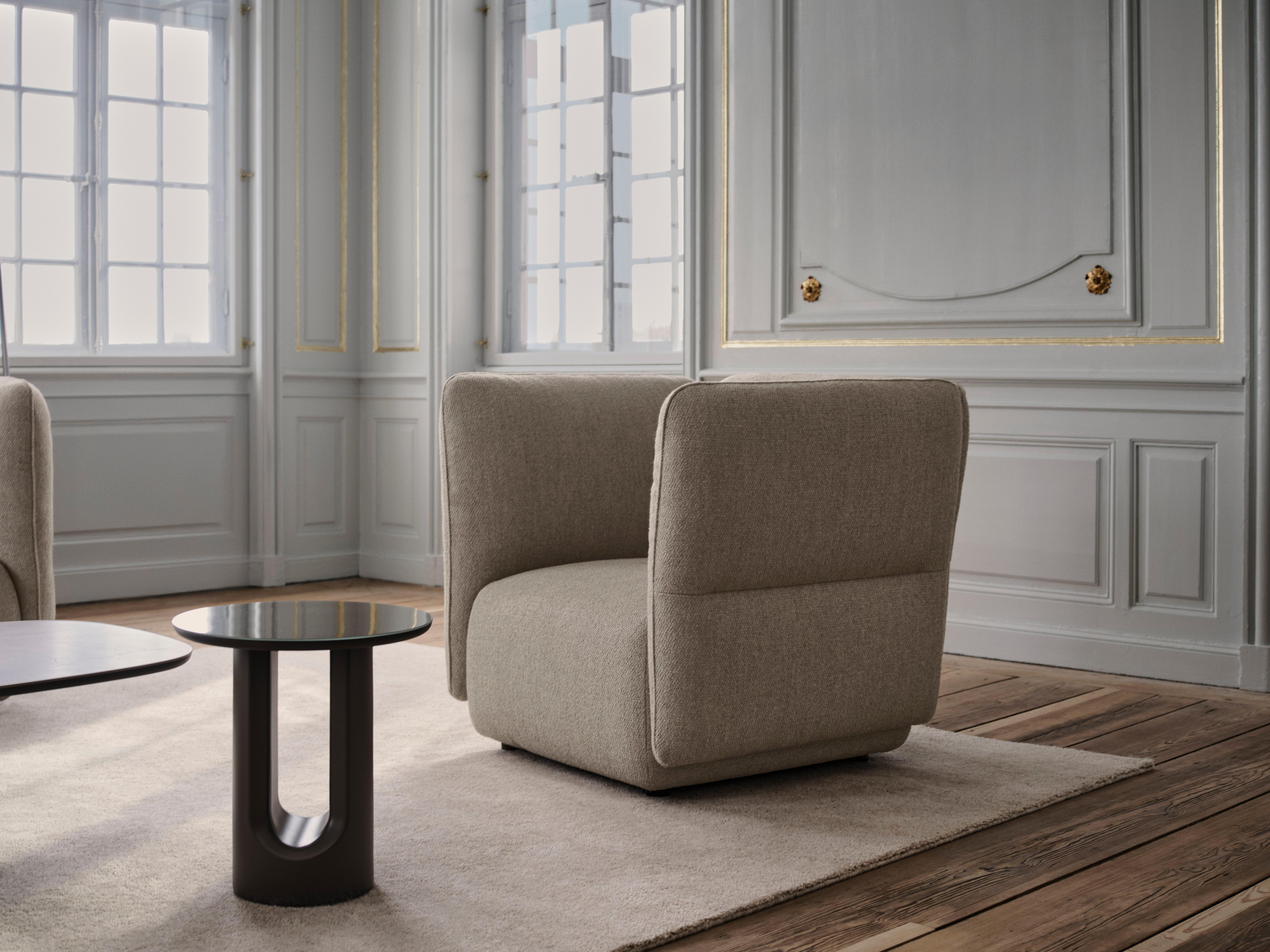 Beige upholstered lounge chair beside round black side tables on a rug.