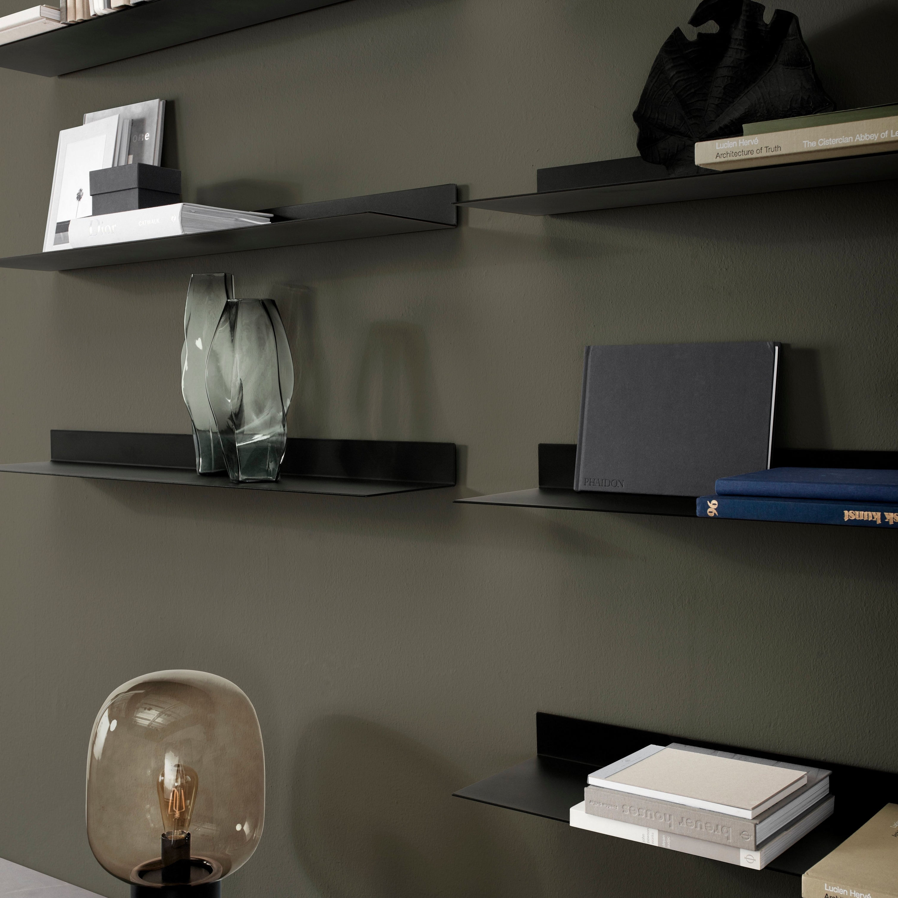Dark wall with floating shelves displaying books, decorative items, and a unique table lamp.