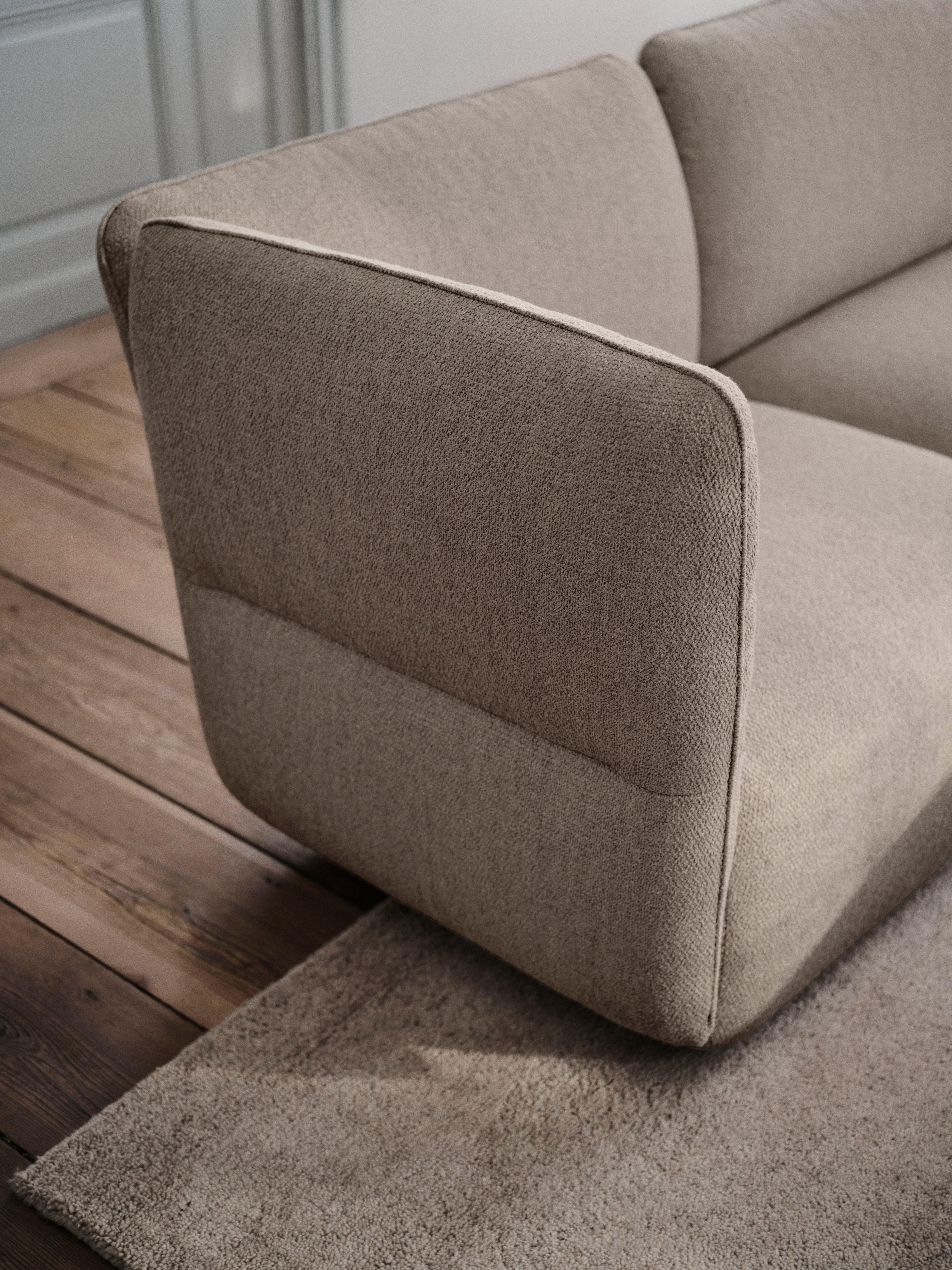 Close-up of upholstered sofa armrest and back cushion with piping detail.