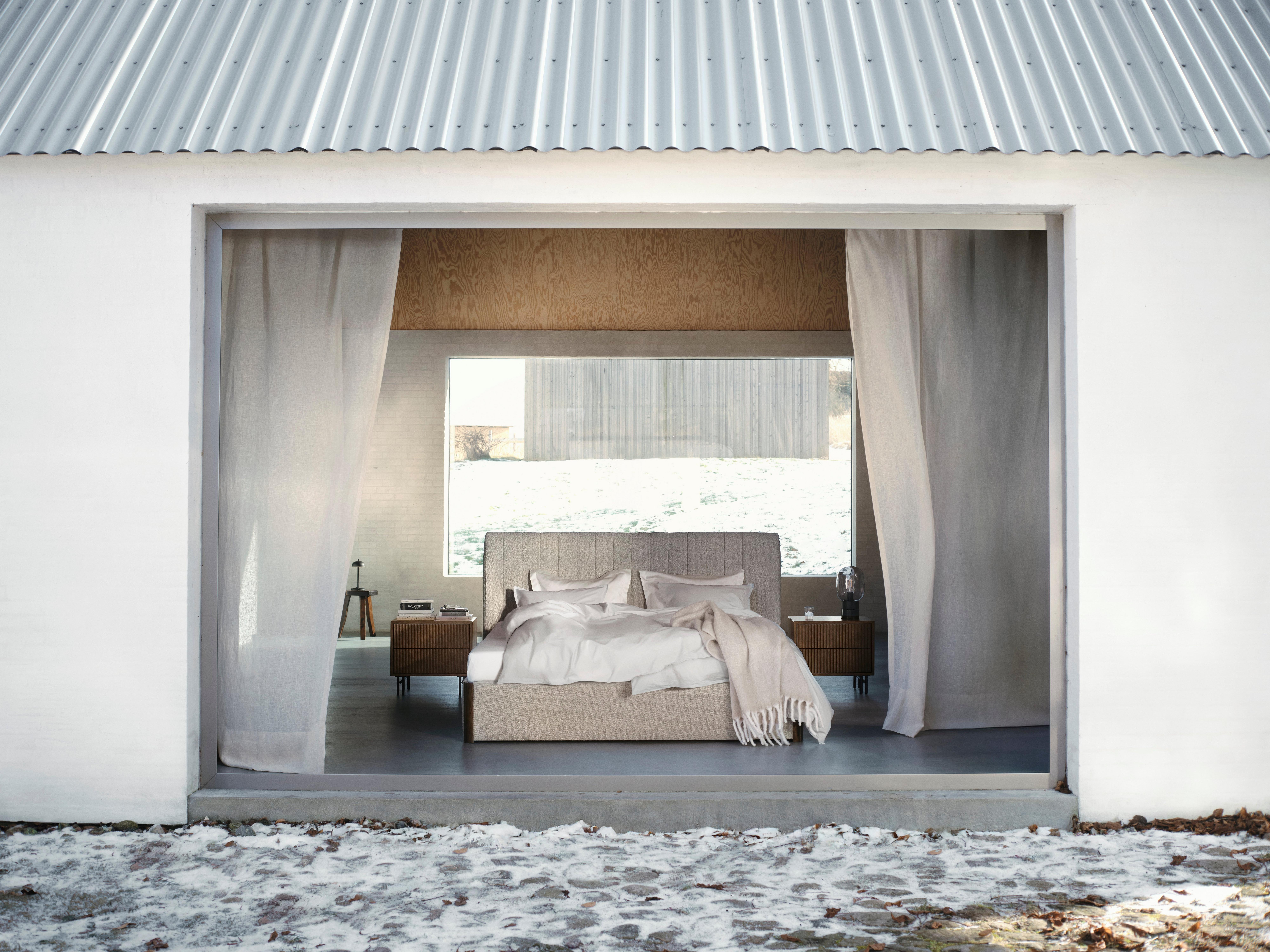 Modern bedroom with soft bedding and neutral tones, featuring a small side table.