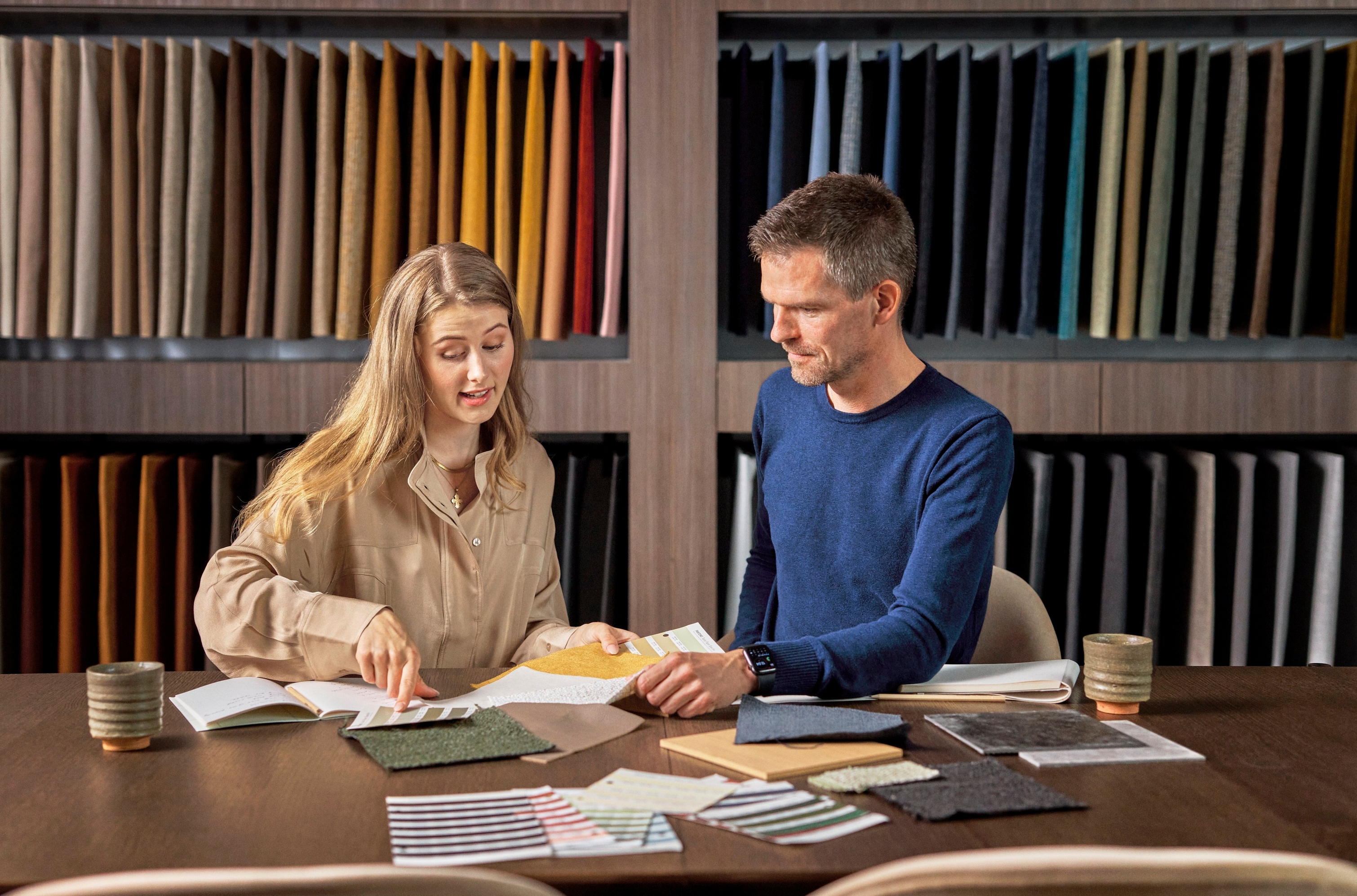 Two people examining fabric samples at a table with color swatches in the background.