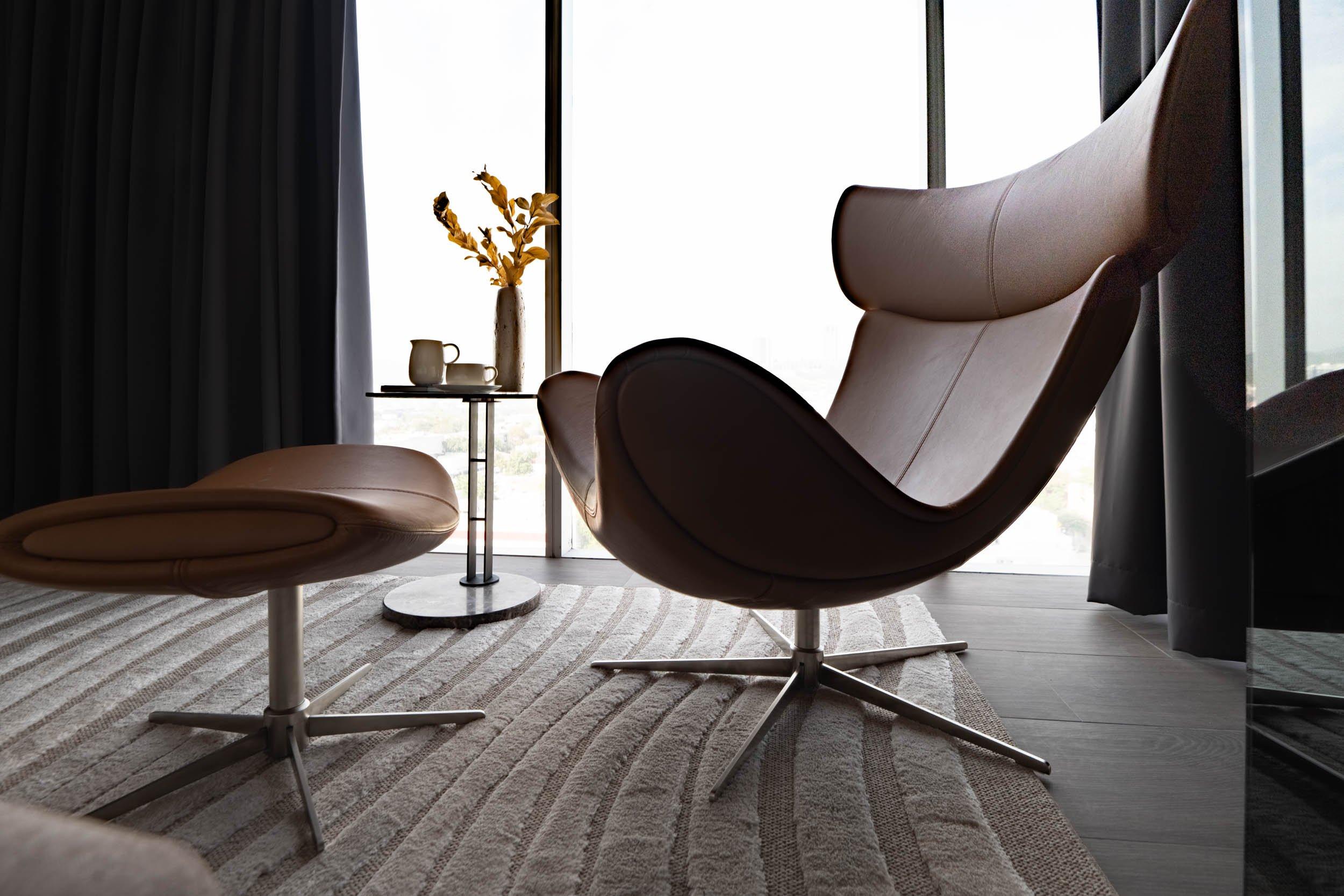 Fauteuil lounge en cuir avec repose-pieds, près d’une table d’appoint avec tasses et vase.