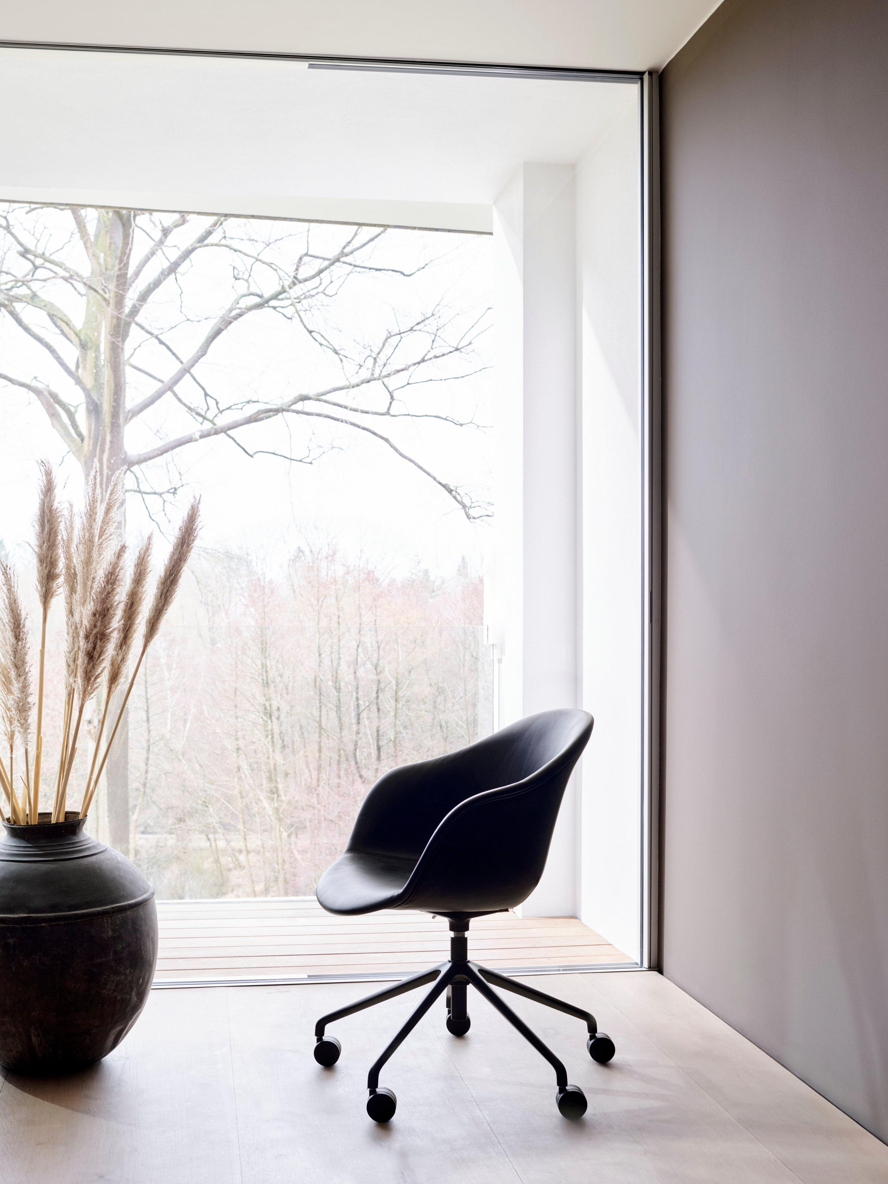 Black swivel chair by large window, decorative vase with pampas grass beside it.