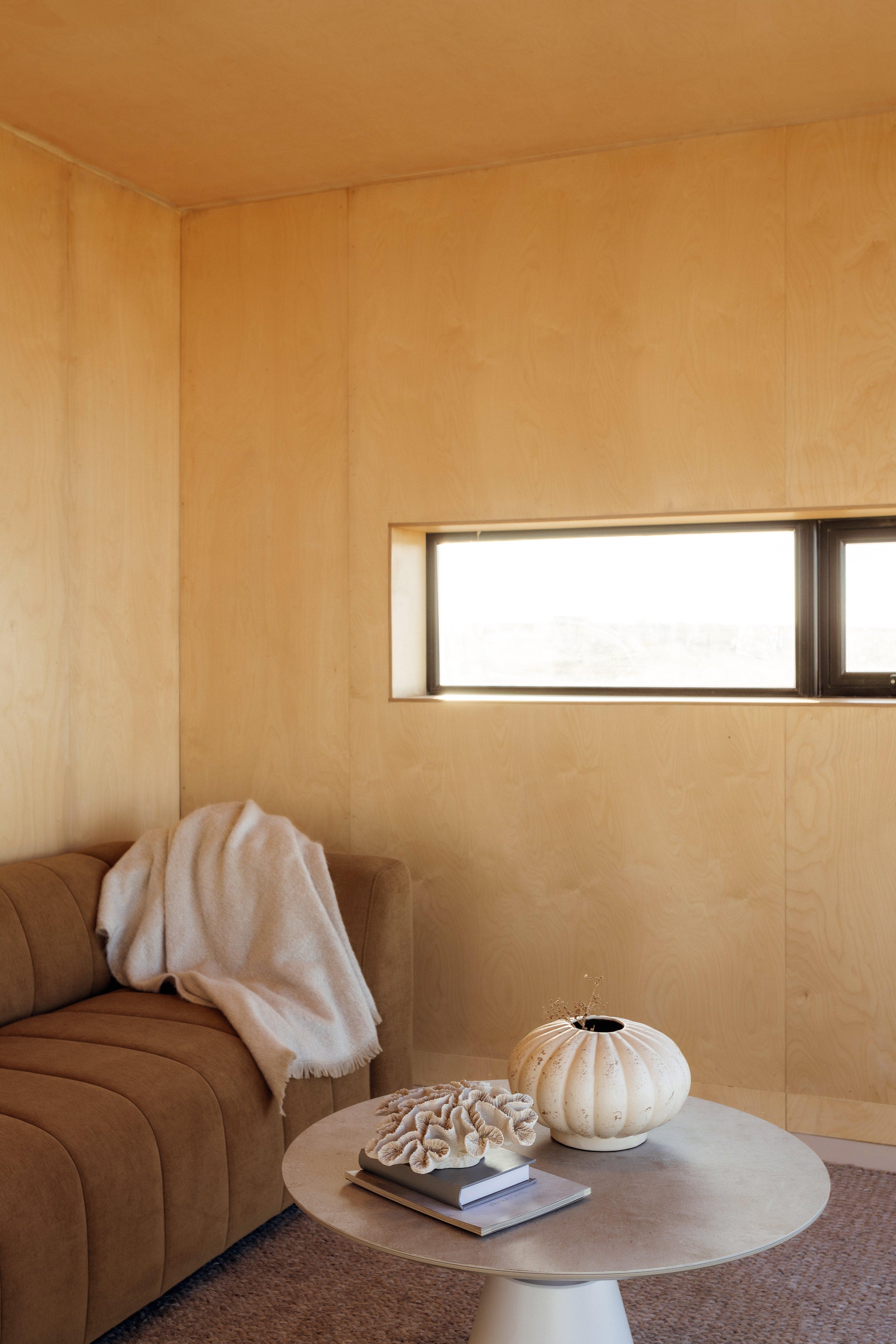 棕色沙發上有毯子，圓形桌上擺放著書、裝飾品和花瓶。