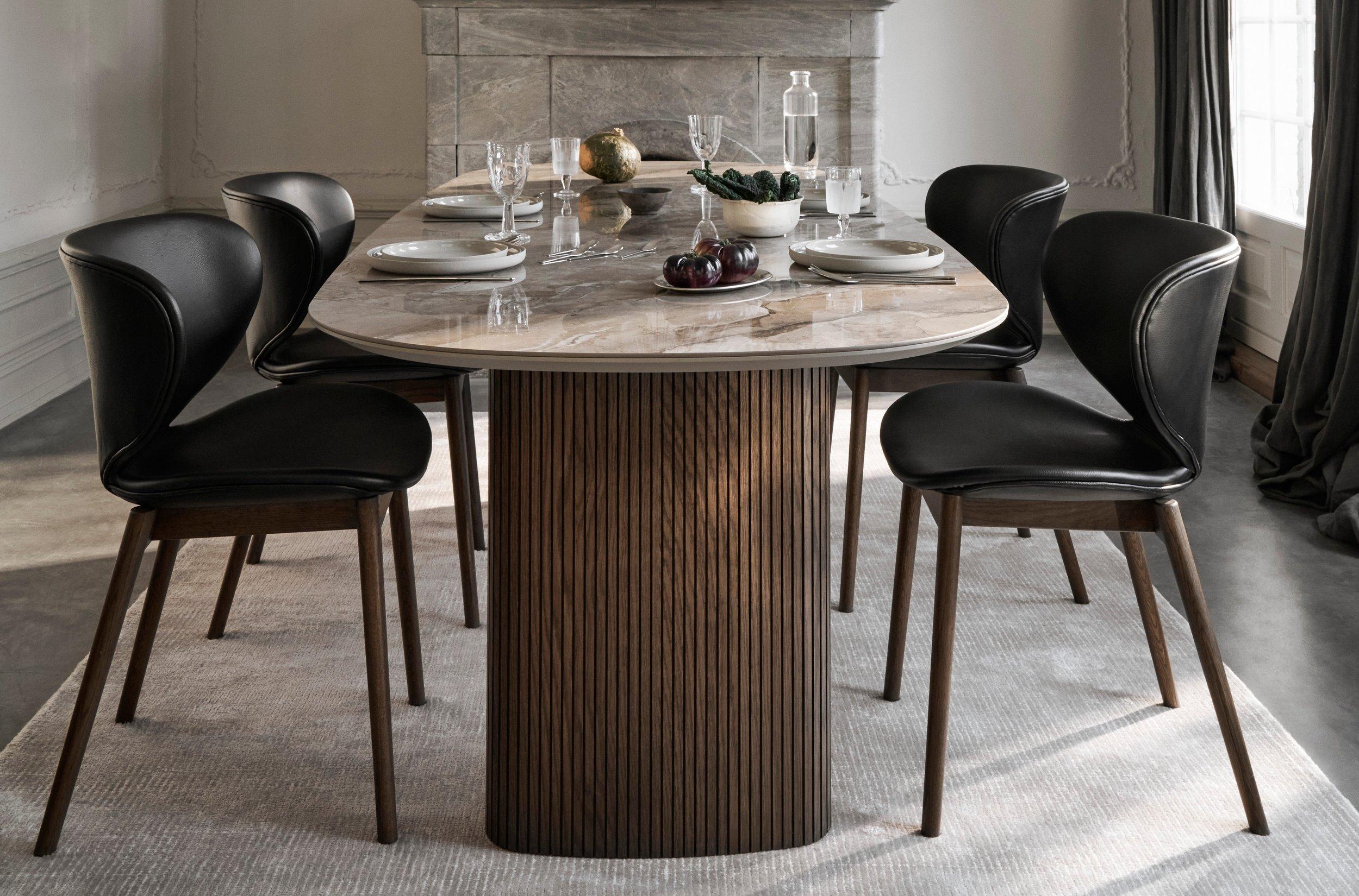 天板が大理石のテーブルに、ブラックのレザーチェアが6脚、装飾的な暖炉があり、明るい色のラグの上には背の高いキャンドルが飾られている、エレガントなダイニングルーム。