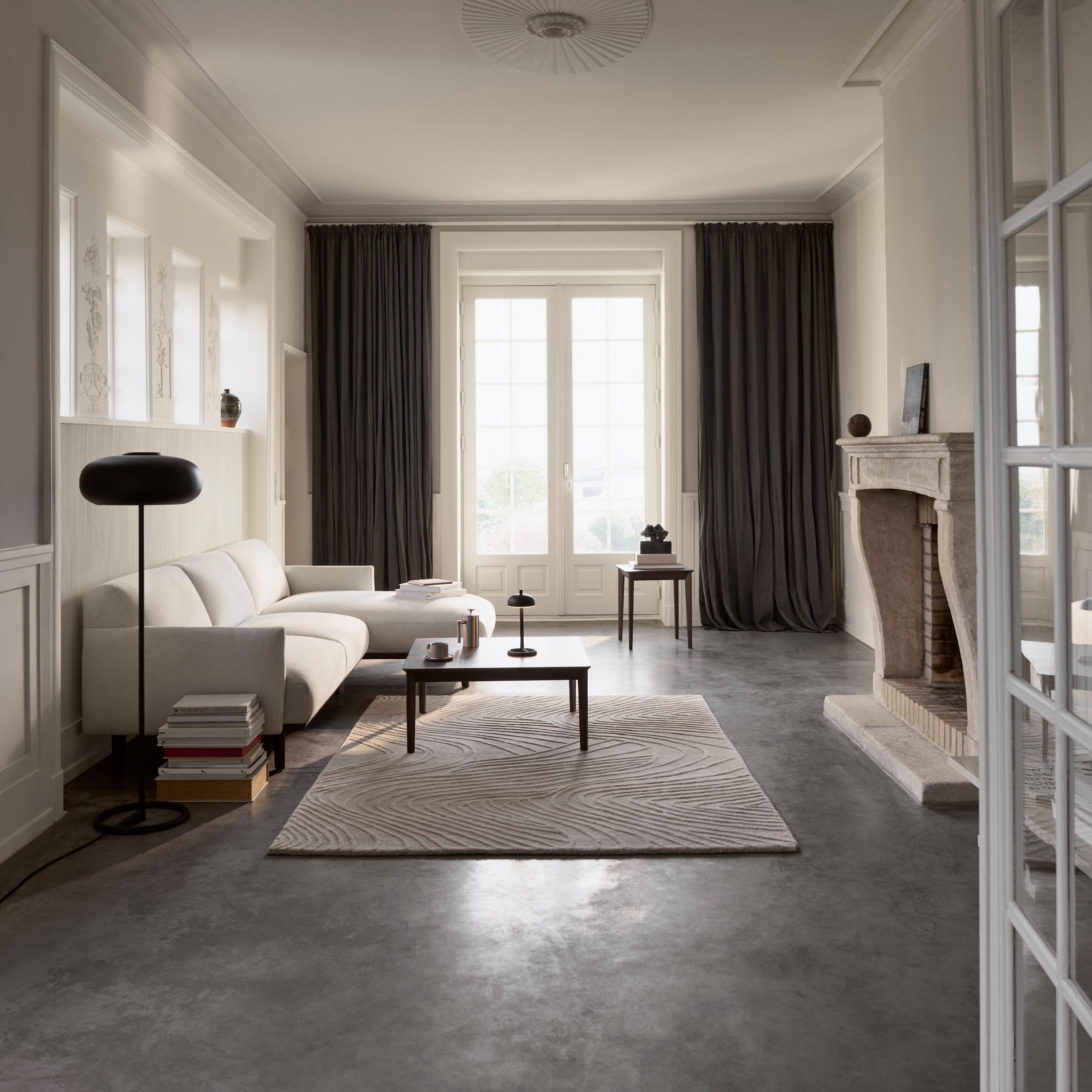 Minimalist living room with light sofa, dark oak coffee and side tables, black floor and table lamps, and natural-tone textured rug.