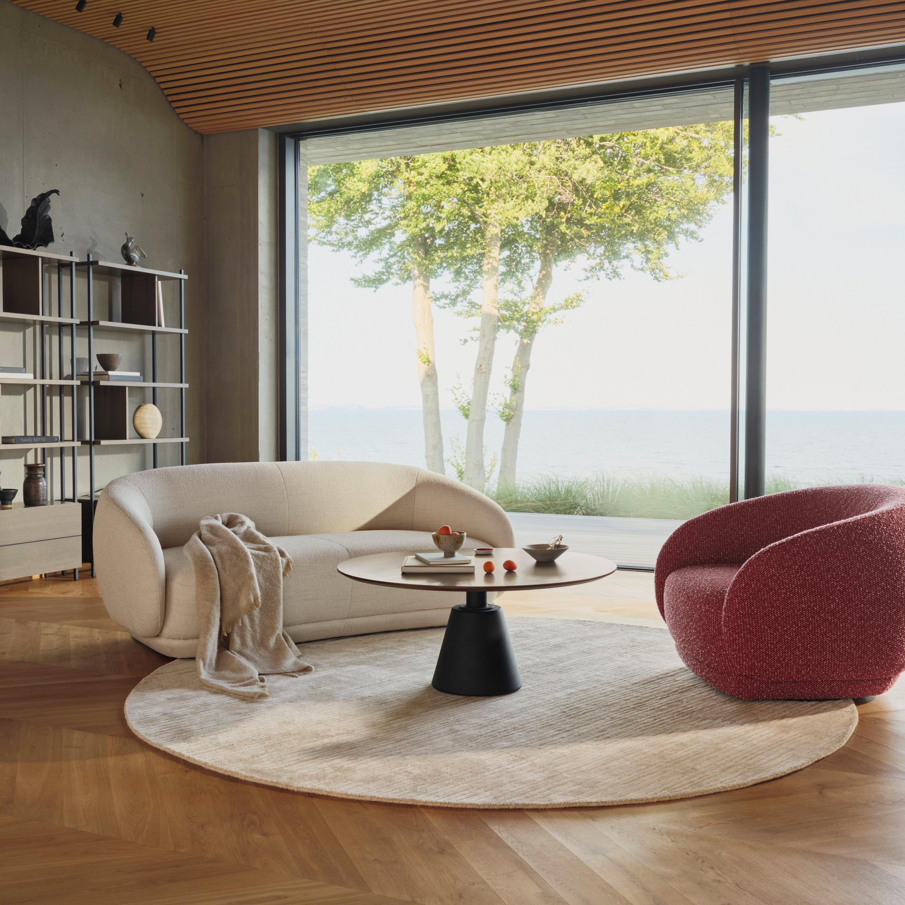 Modern living room with beige sofa, red armchair, round table, and large window with sea view.
