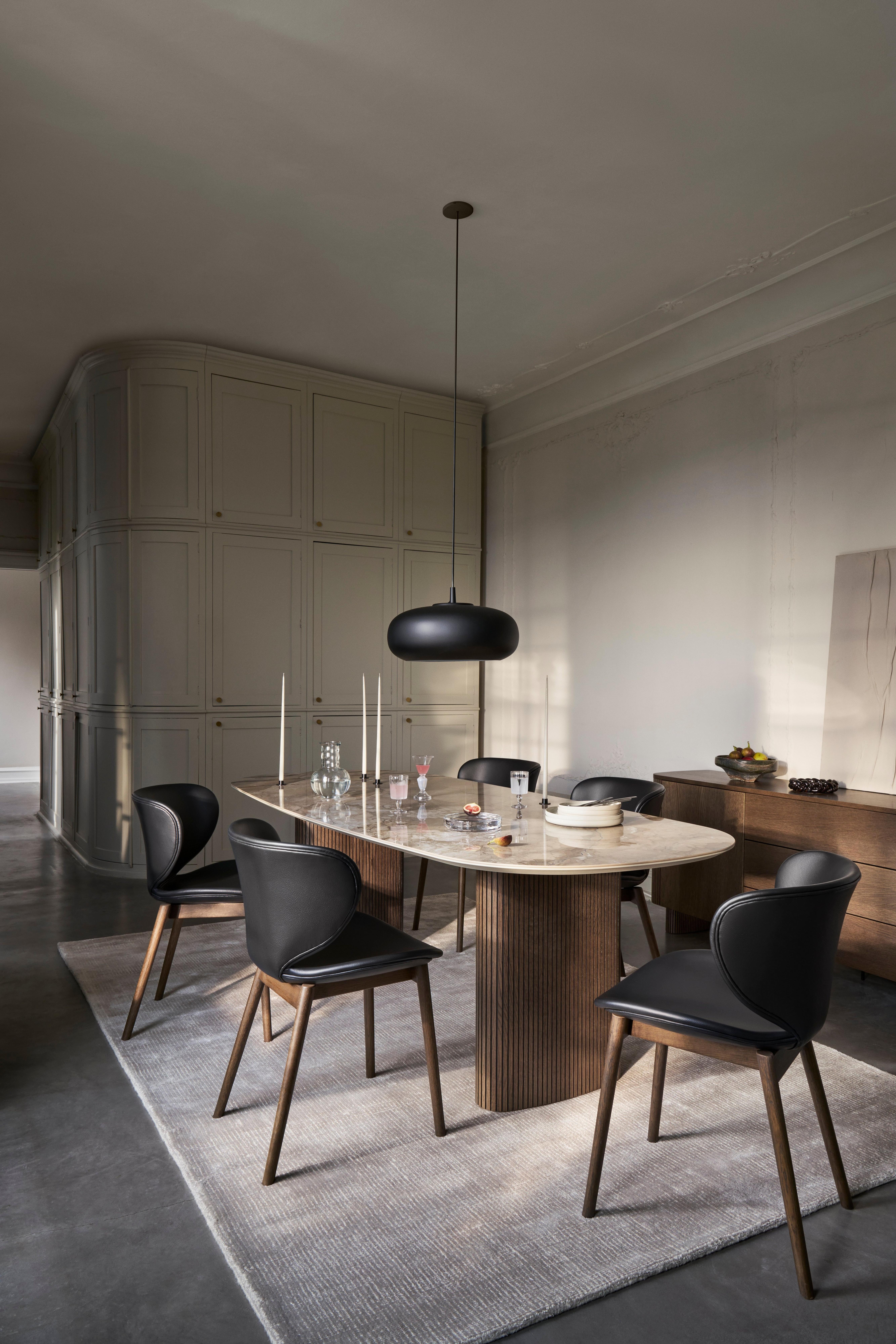 Moderne spisestue med ovalt bord, sorte stole og pendellampe. Dekoreret med glas og lys.