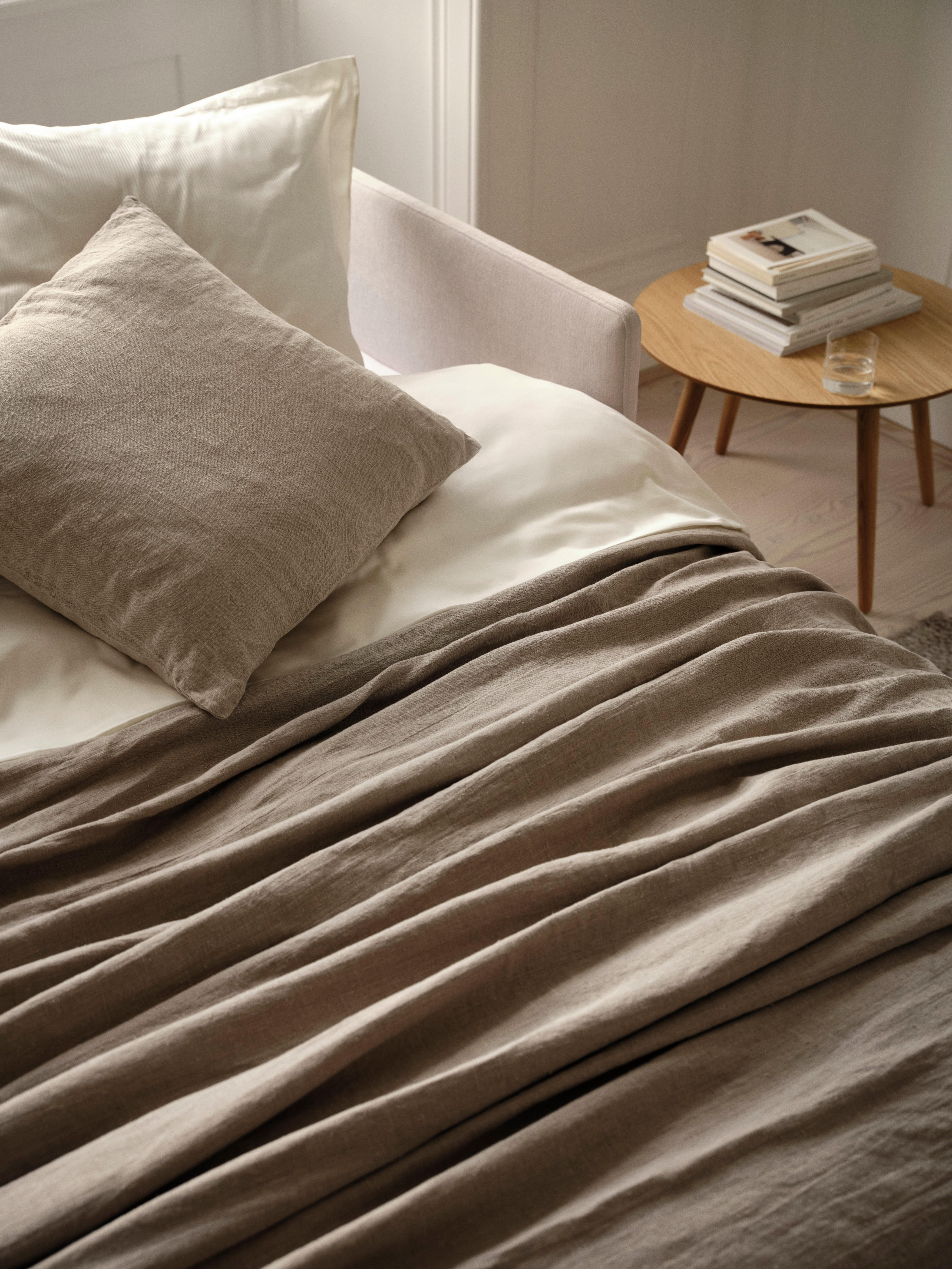 Bed with beige pillow and blanket; nearby a round table with stacked books and a glass.