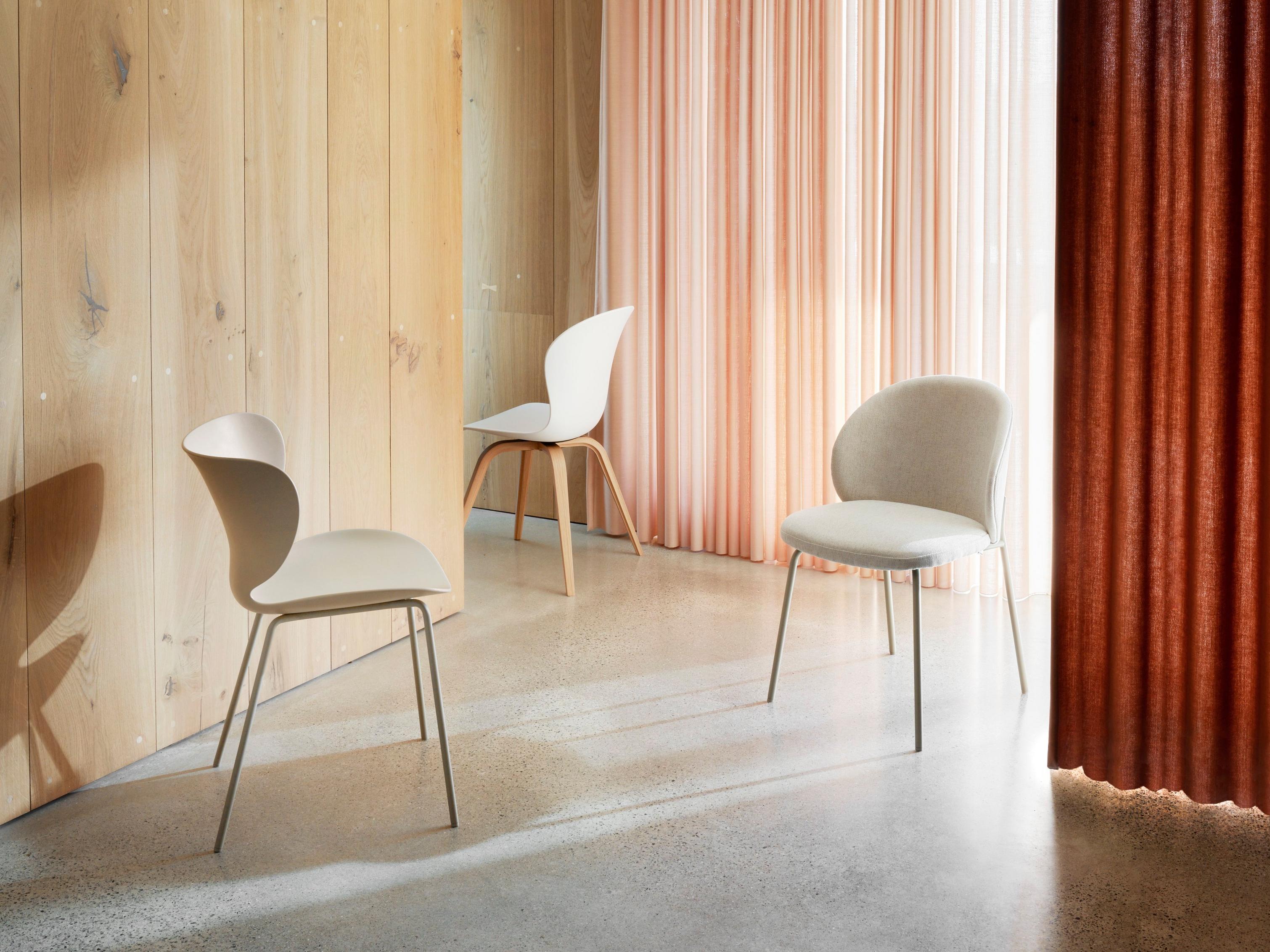 Cadeiras modernas numa divisão com parede de madeira e cortina drapeada em vermelho coral.