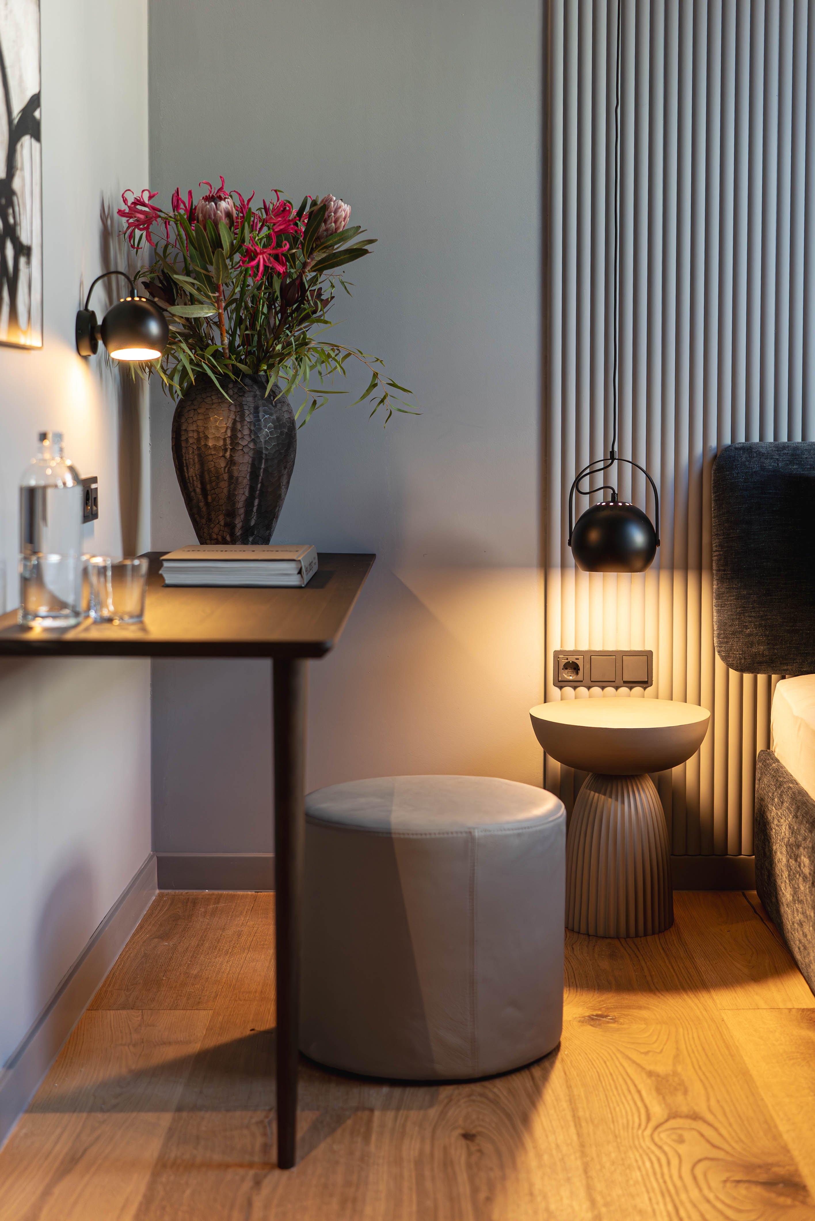 Table avec vase fleuri, livre, lampe murale et tabouret rond.