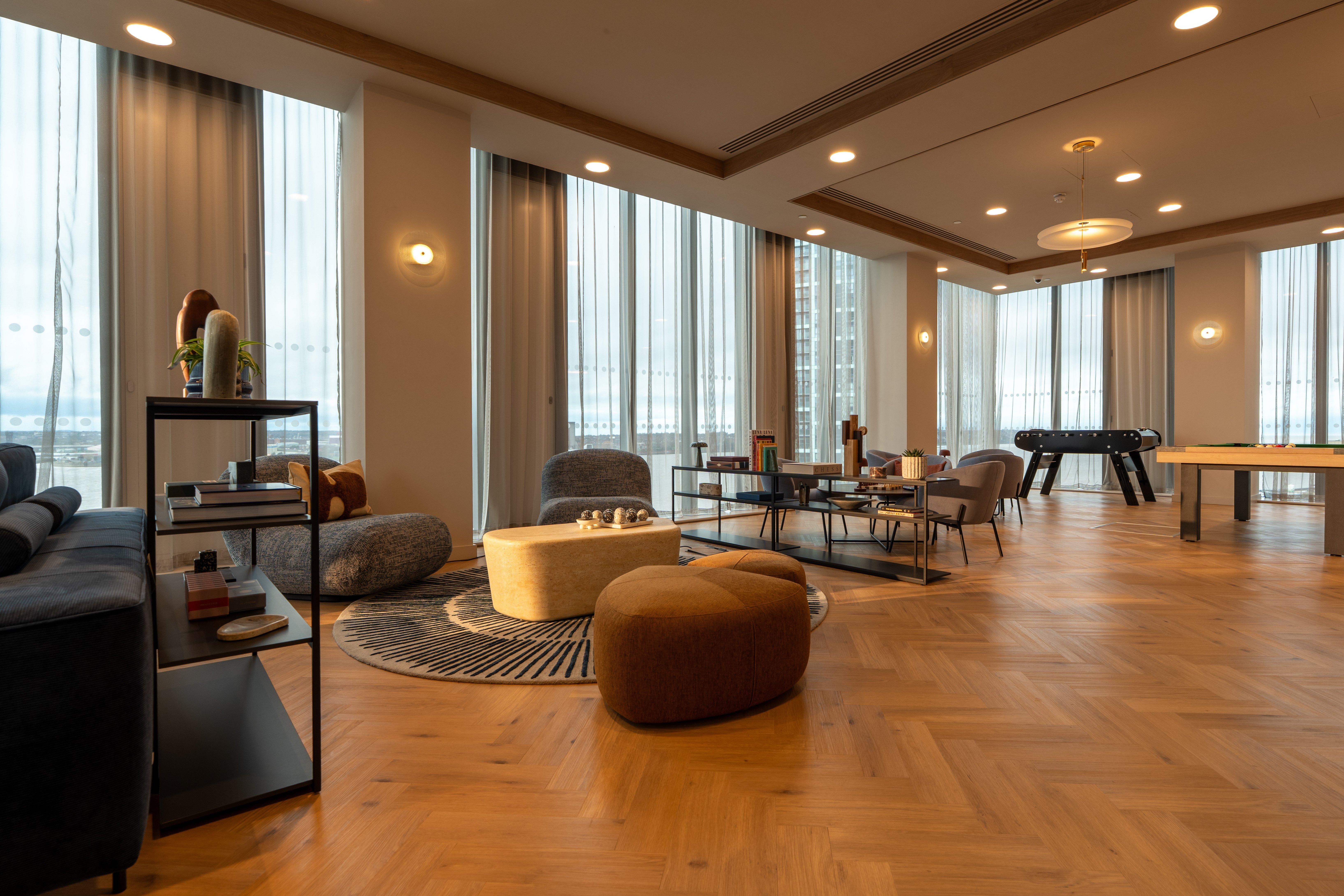 Sala de estar moderna con sofás, pufs, mesa baja y mesa de billar junto a ventanales.