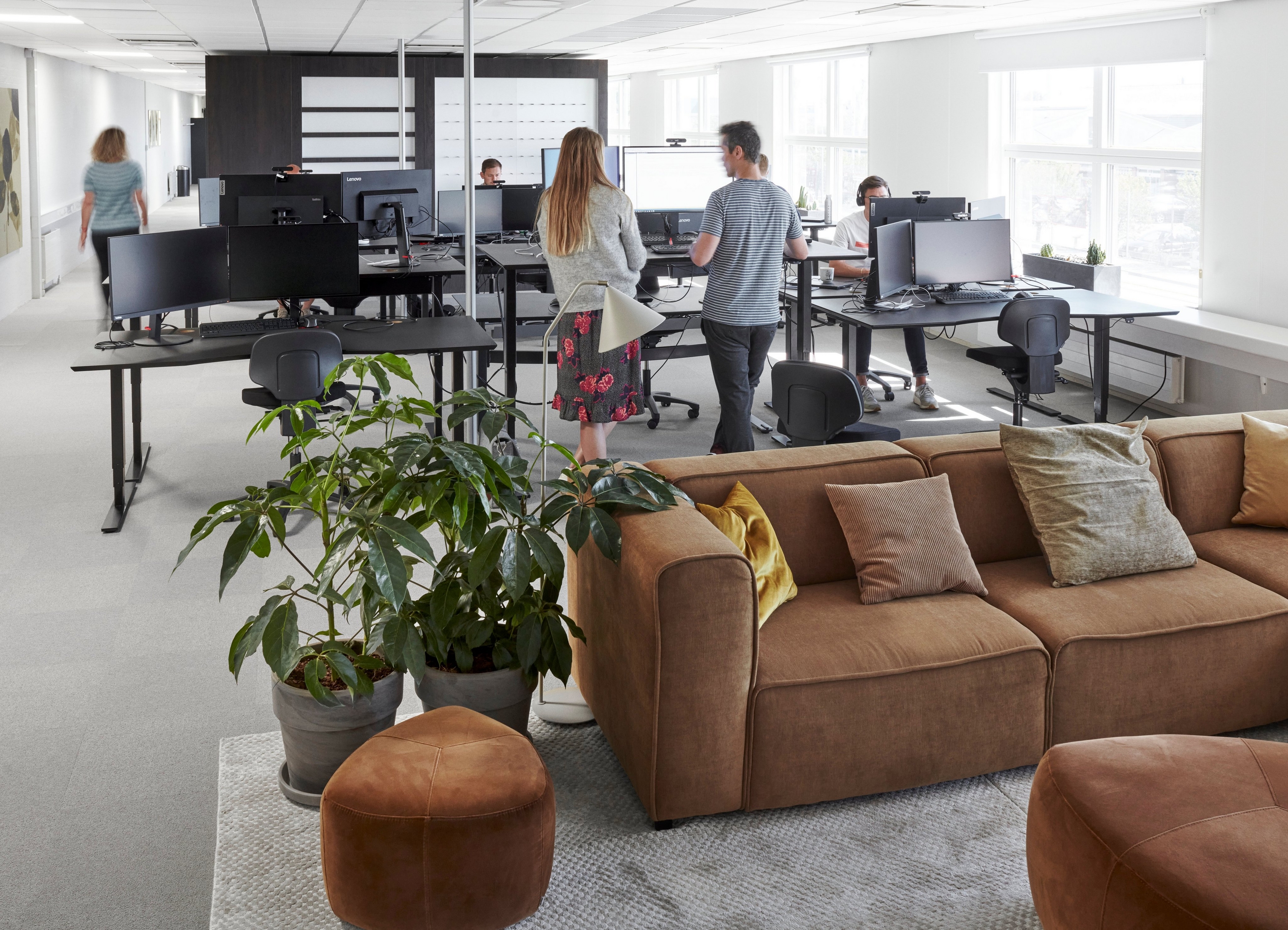 BoConcept propose un siège social moderne avec des employés, des ordinateurs, des plantes et un canapé Carmo marron.