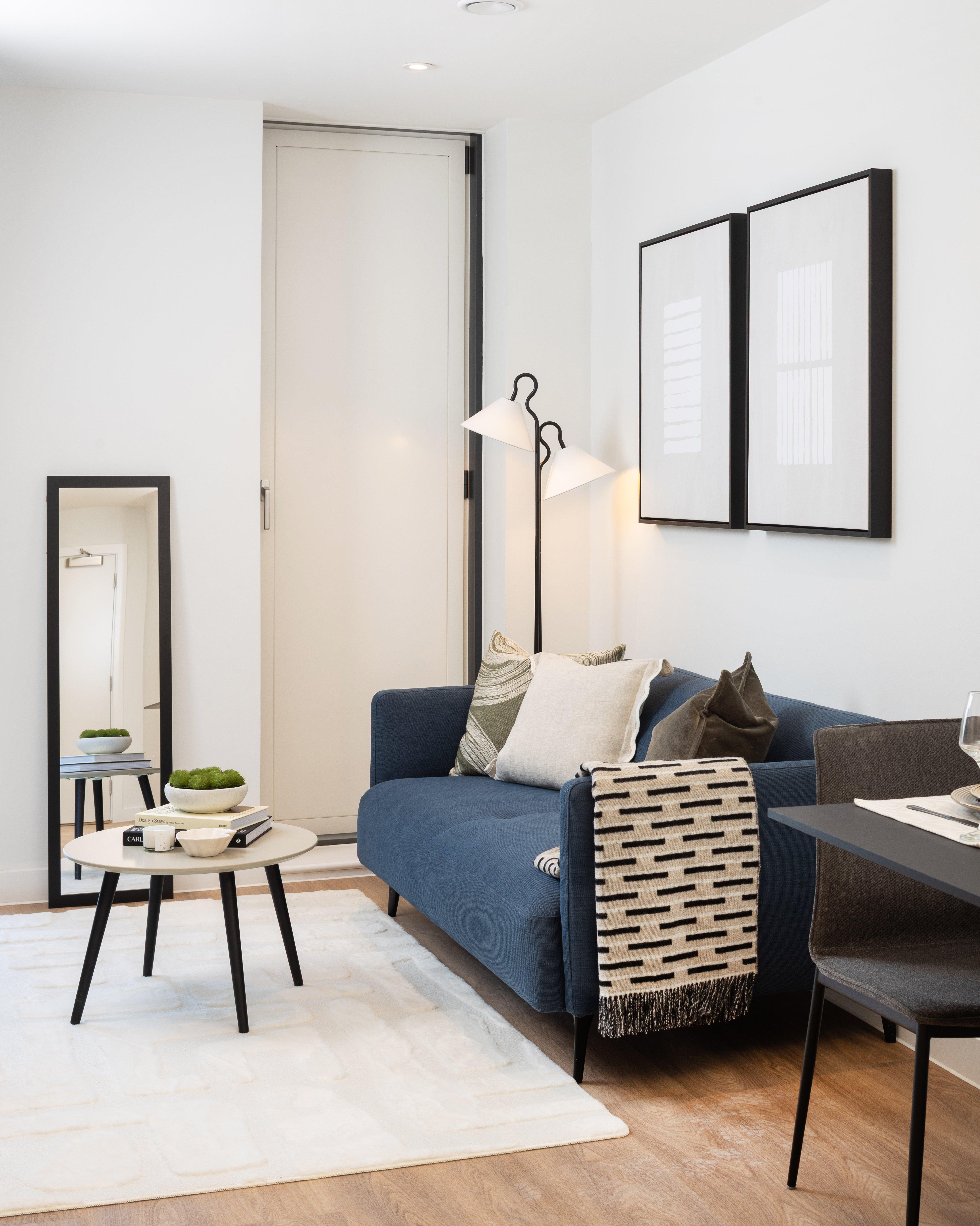 Salón con sofá azul, lámpara de pie, mesa auxiliar y espejo de pared.