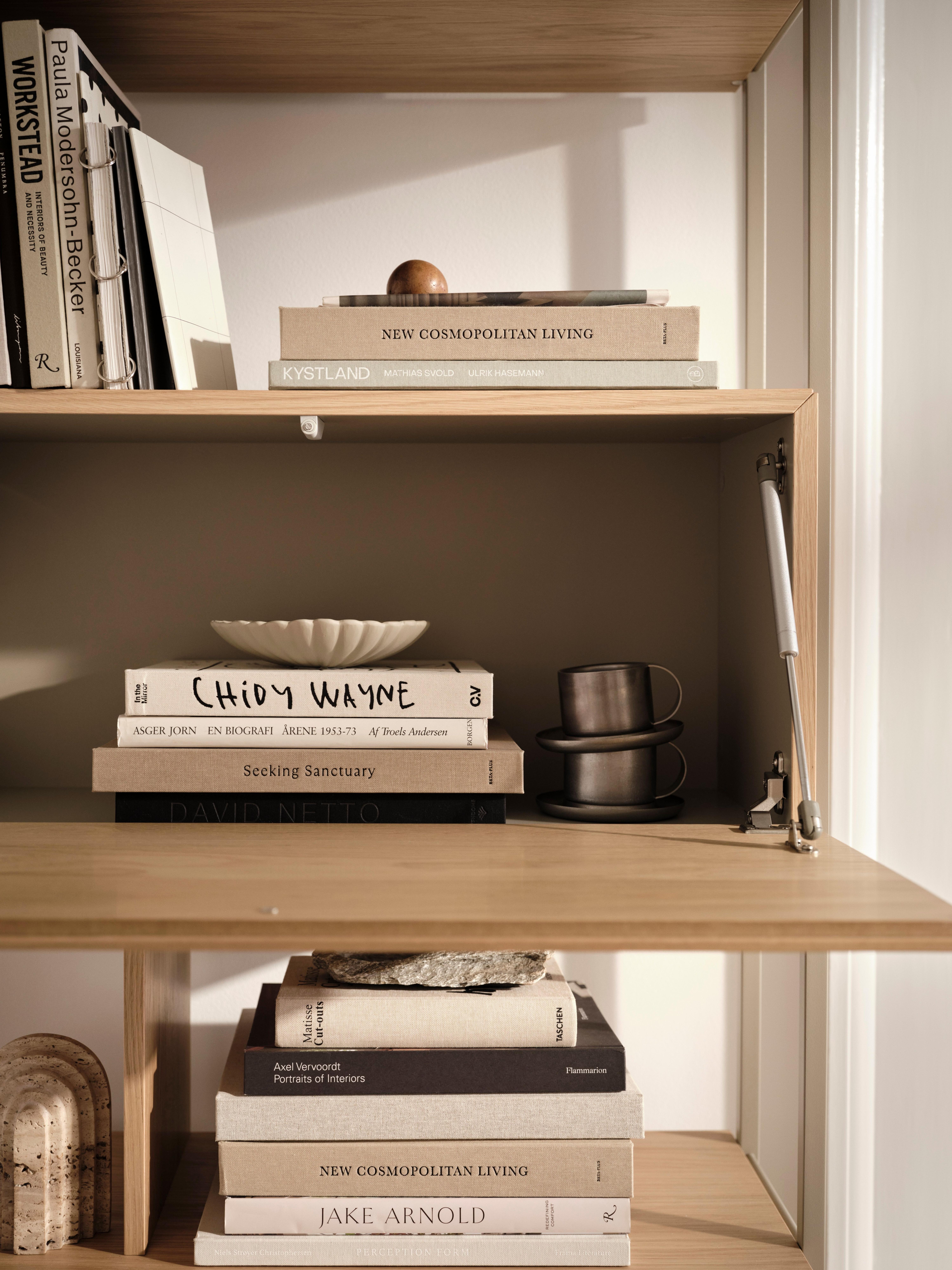 Wooden shelves with stacked books, a white bowl, and two stacked cups.