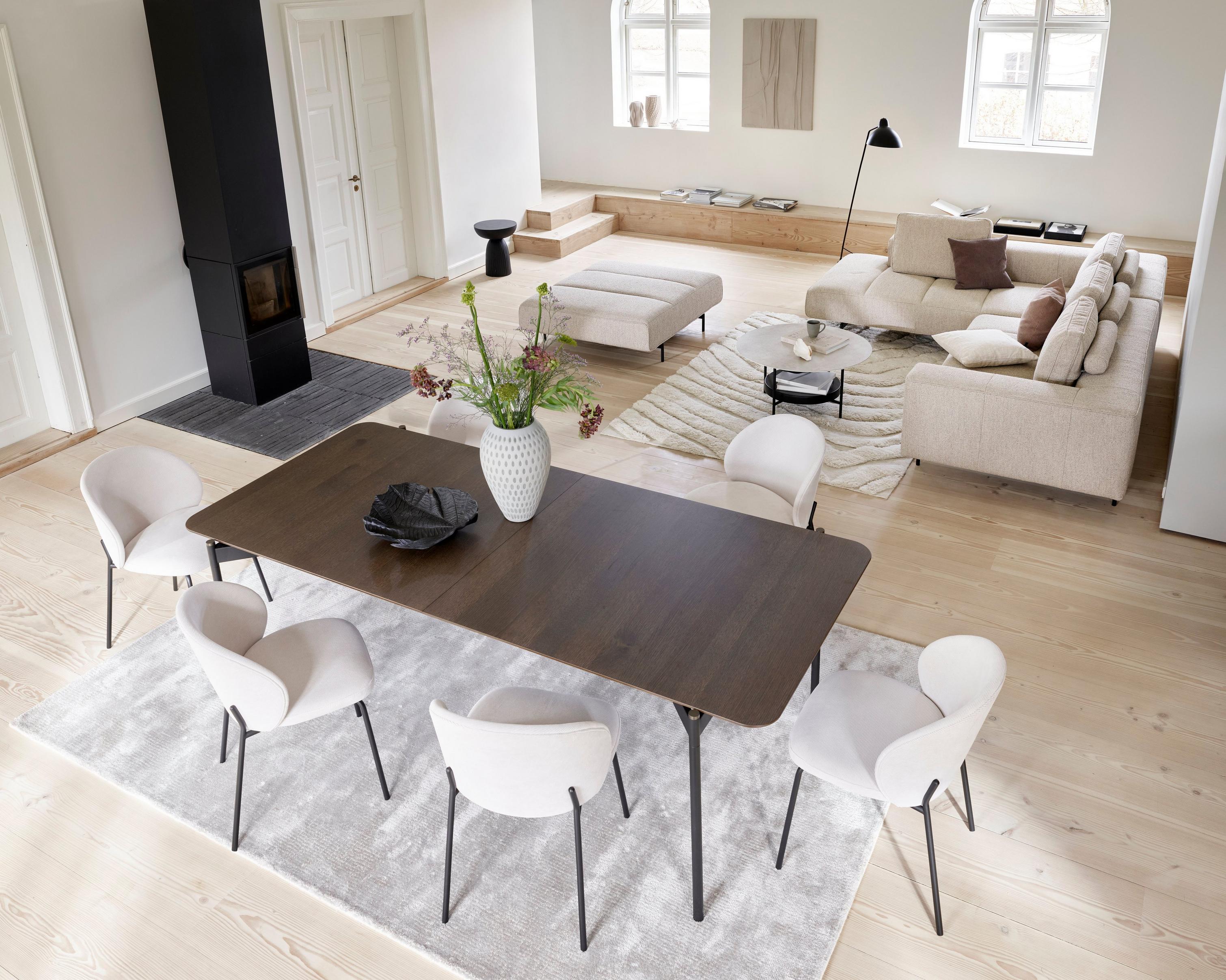 O sofá de canto Amsterdam com módulo relax e apoio de pés em tecido Lazio bege com a mesa Augusta numa sala de estar grande.