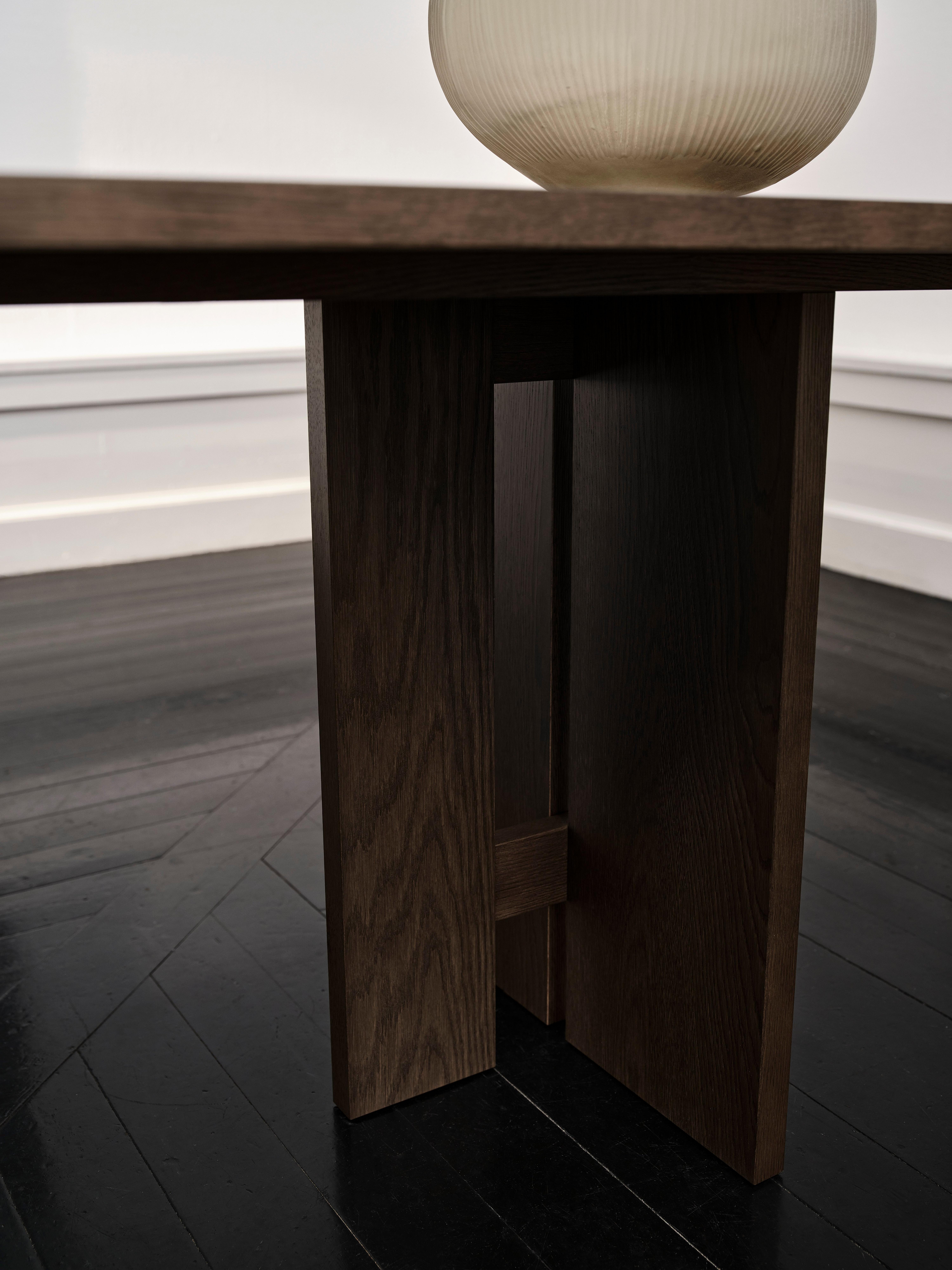 Wooden table leg with a large beige vase on the tabletop. Dark wood flooring visible.