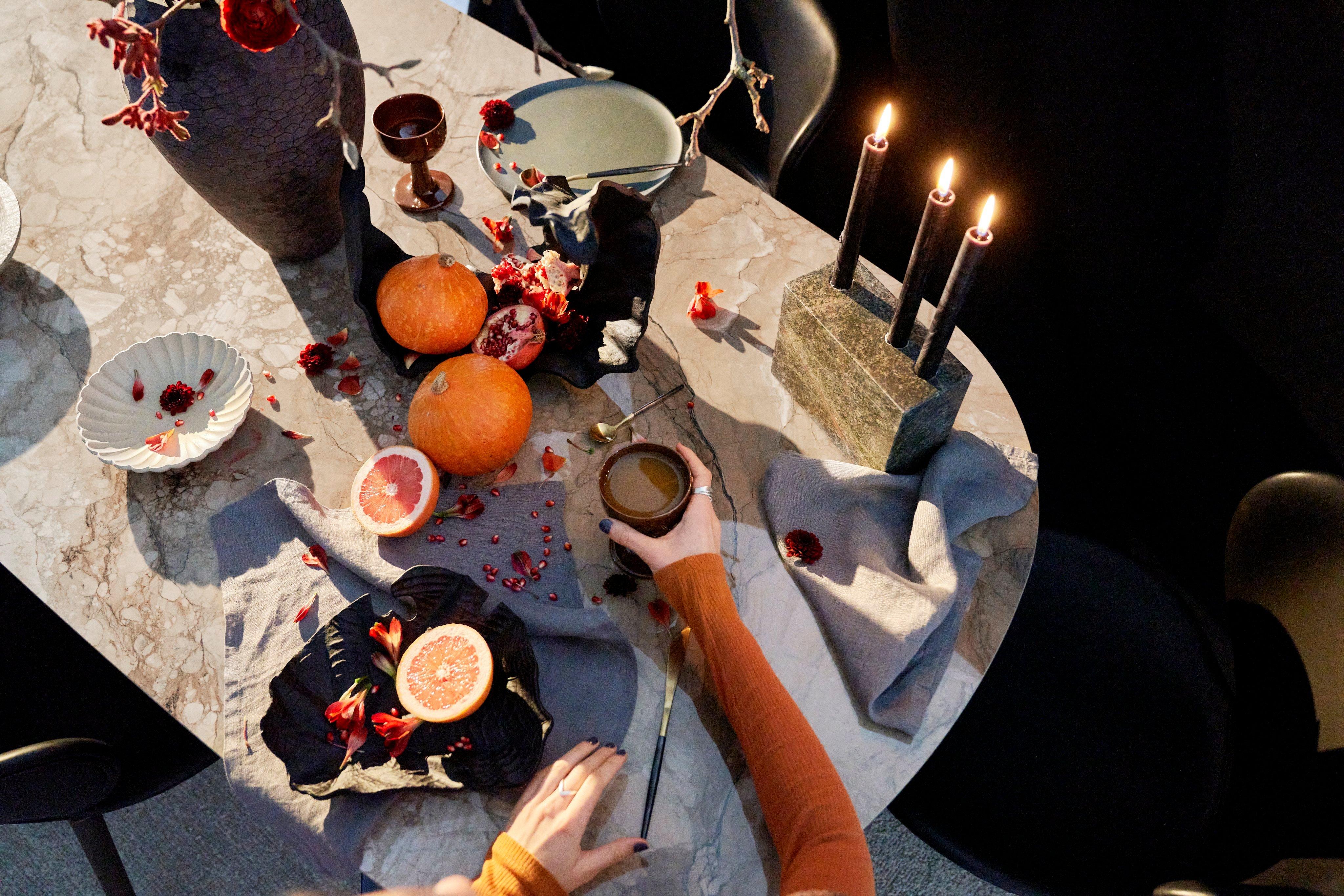 Žena sedící u slavnostně prostřeného jídelního stolu se svíčkami a pomeranči.