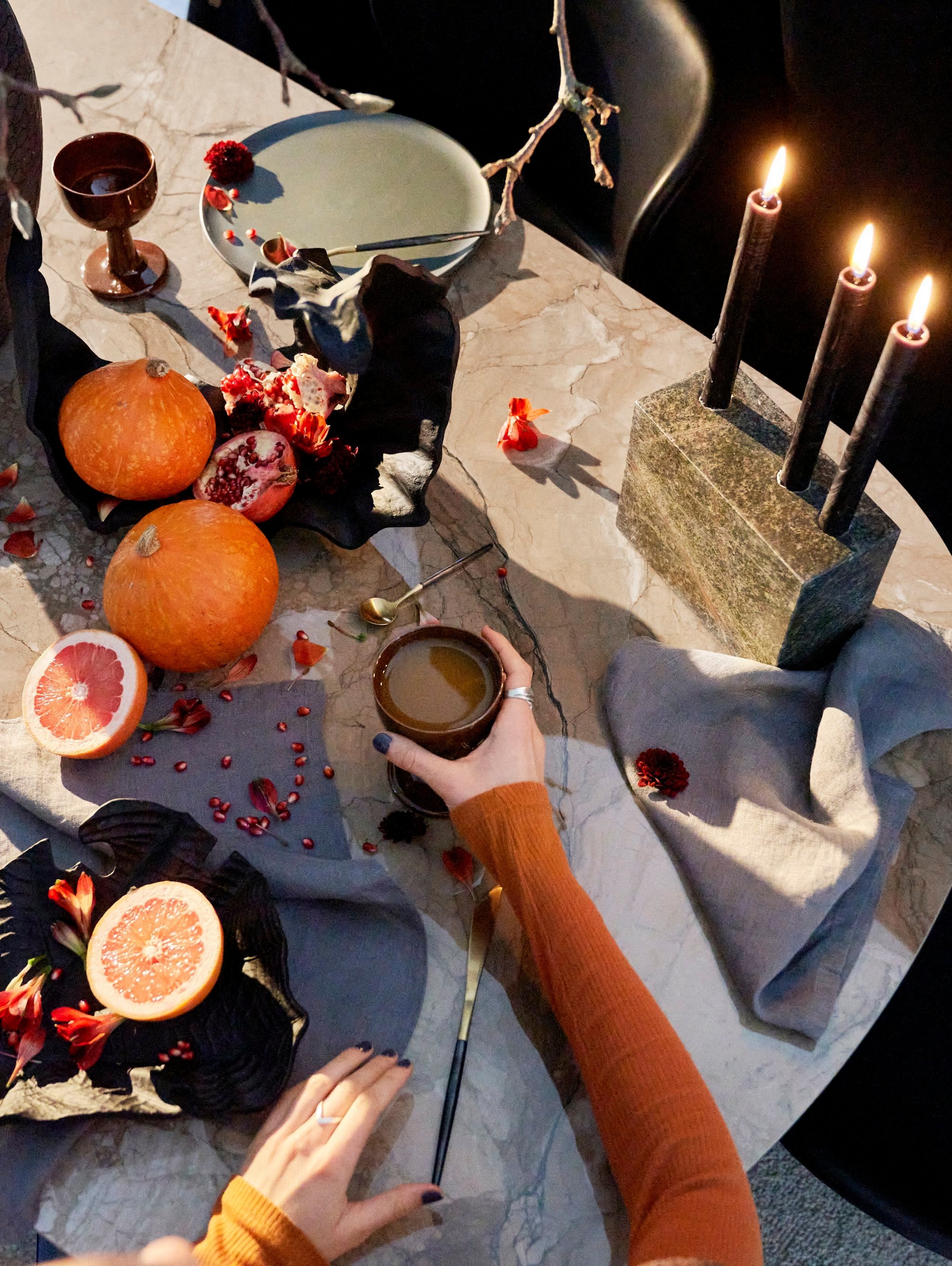Femme assise à une table de repas festive avec des bougies et des oranges.