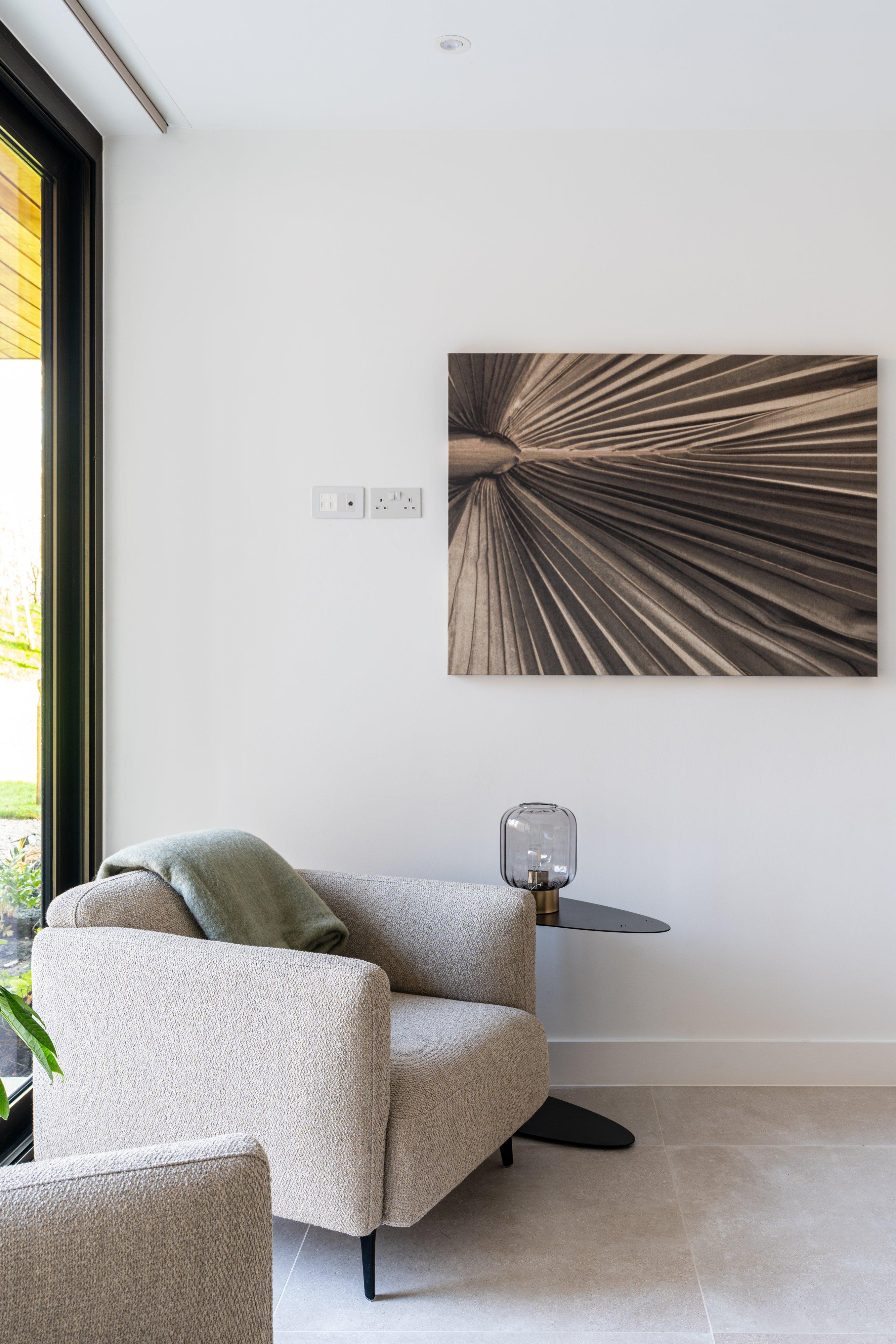Upholstered armchair with a throw and side table holding a glass lamp, beneath wall art.