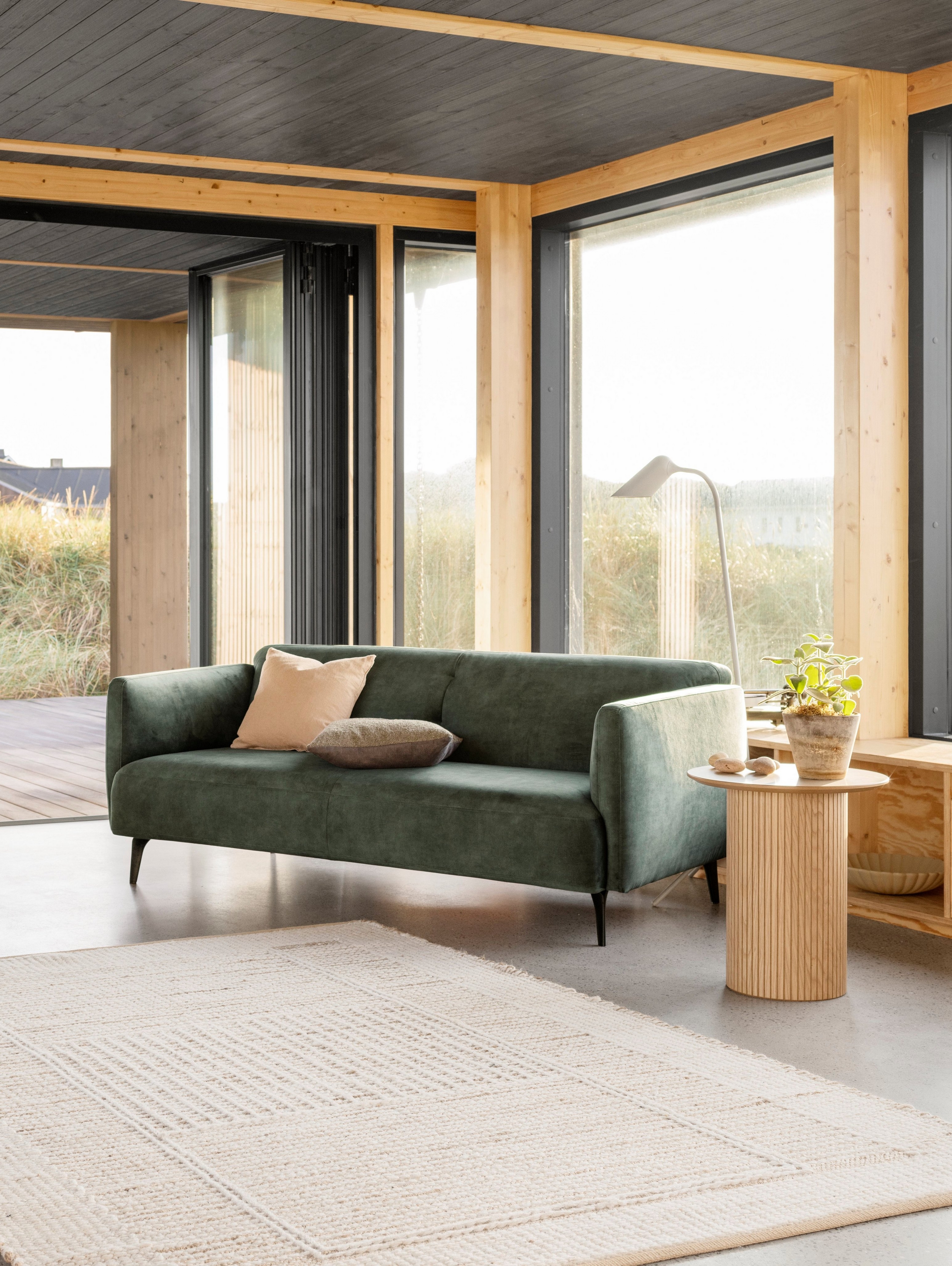 De elegante Modena zitbank en bijpassende fauteuil in groene Ravello stof staan naast een open haard in deze warme woonkamer.