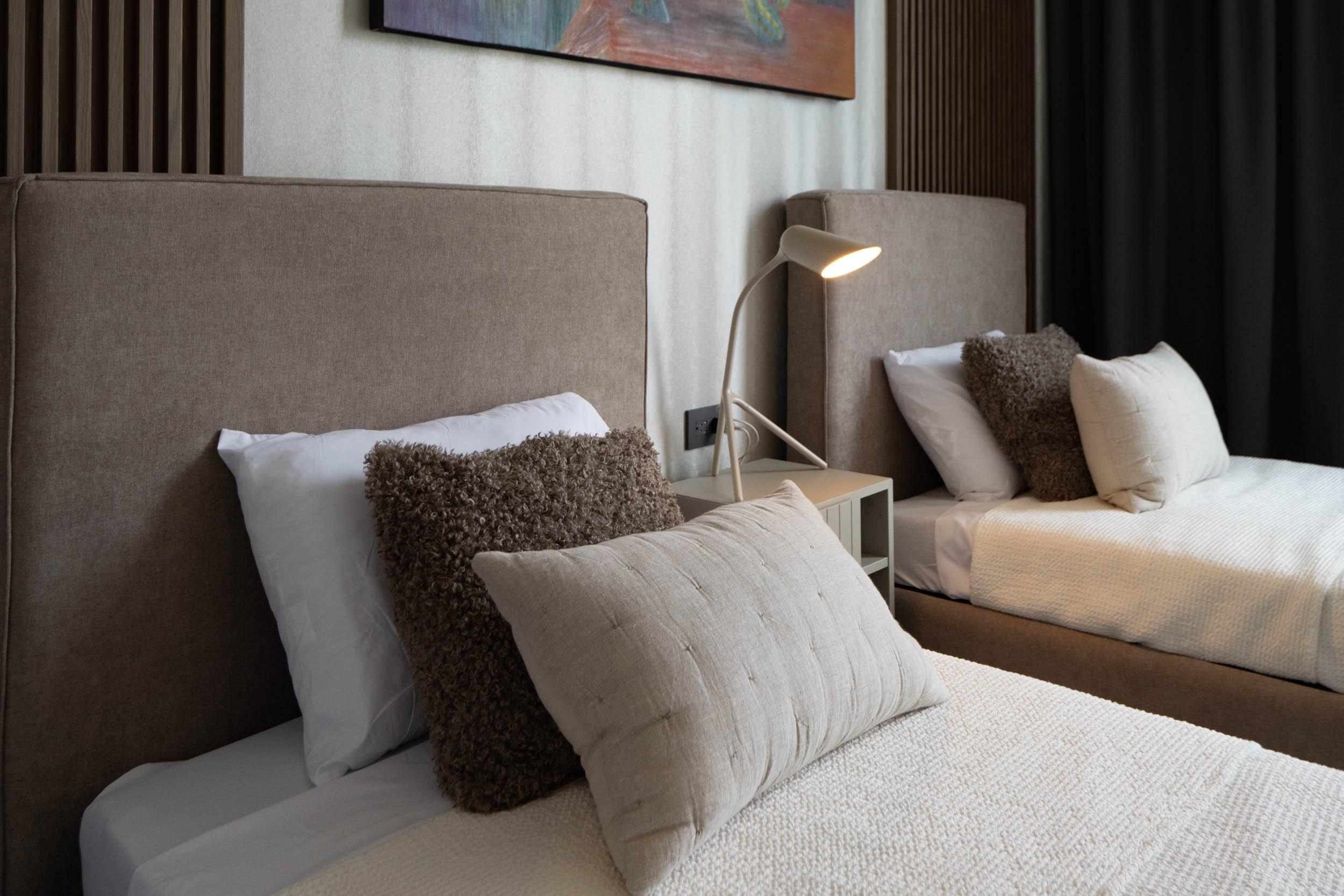 Deux lits simples avec coussins décoratifs et lampe de chevet allumée sur table de nuit.