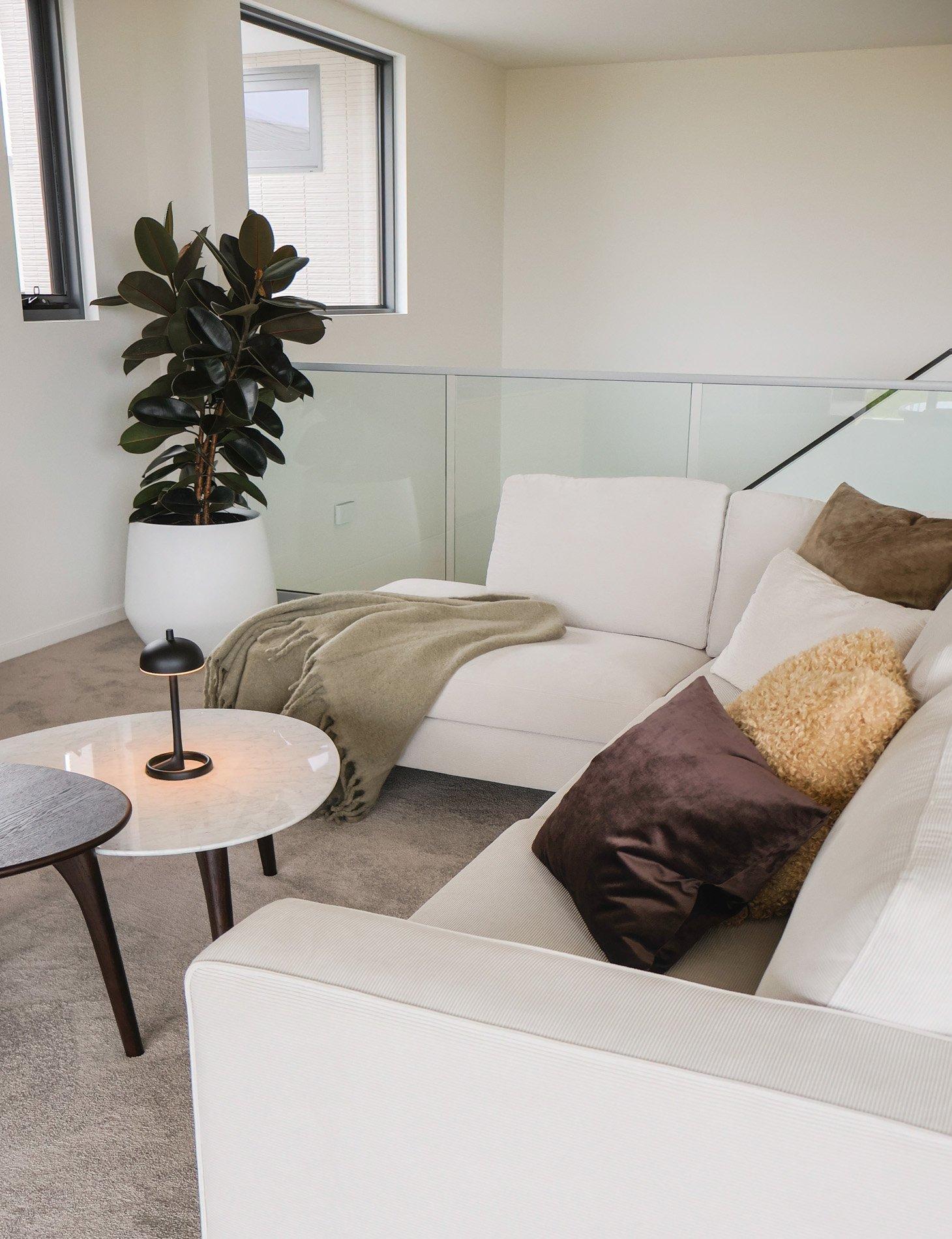 Hvit sofa med fargerike puter, grønt teppe, planter, og to små bord.