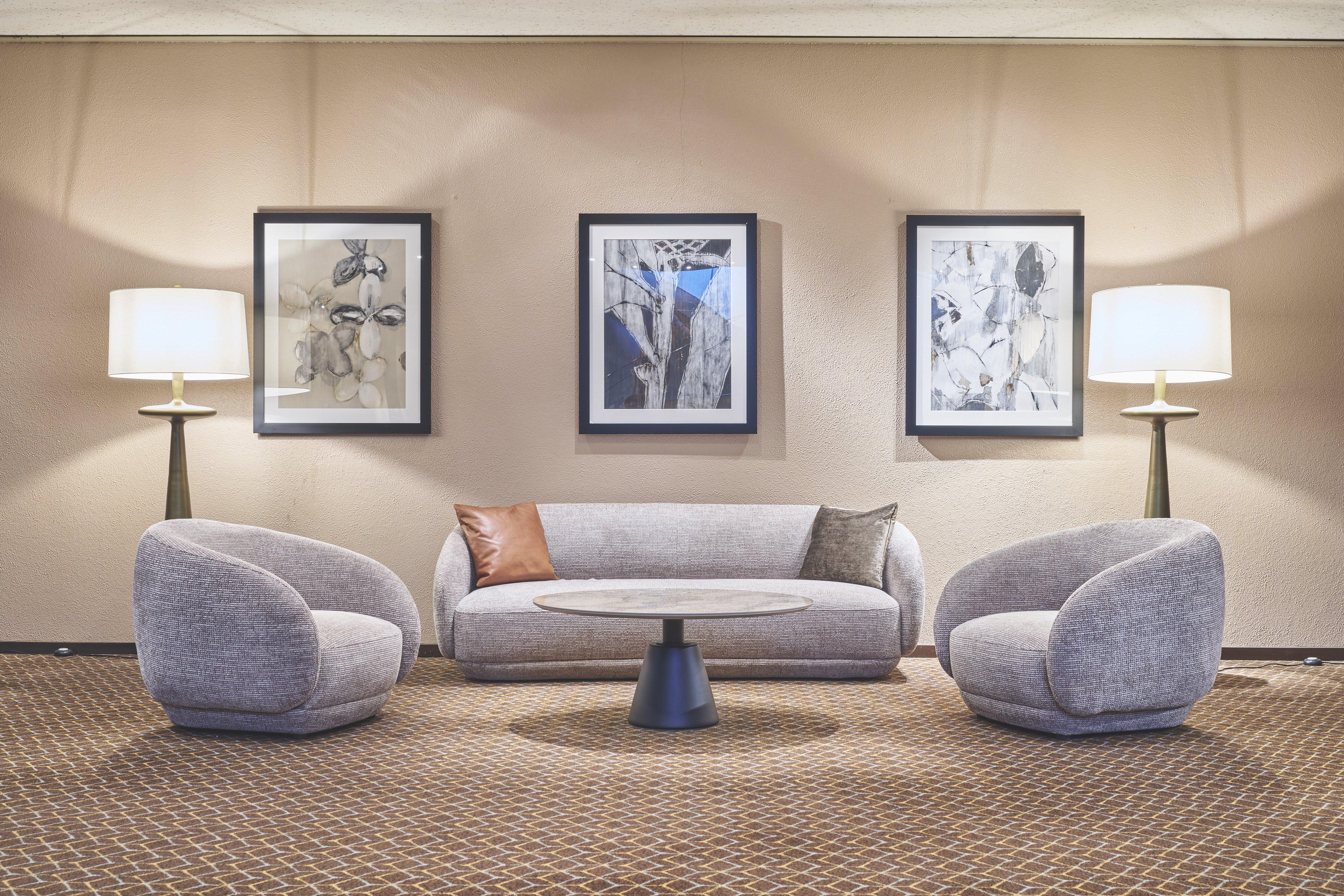 Grey sofa with two armchairs and round coffee table, flanked by two floor lamps and art prints.