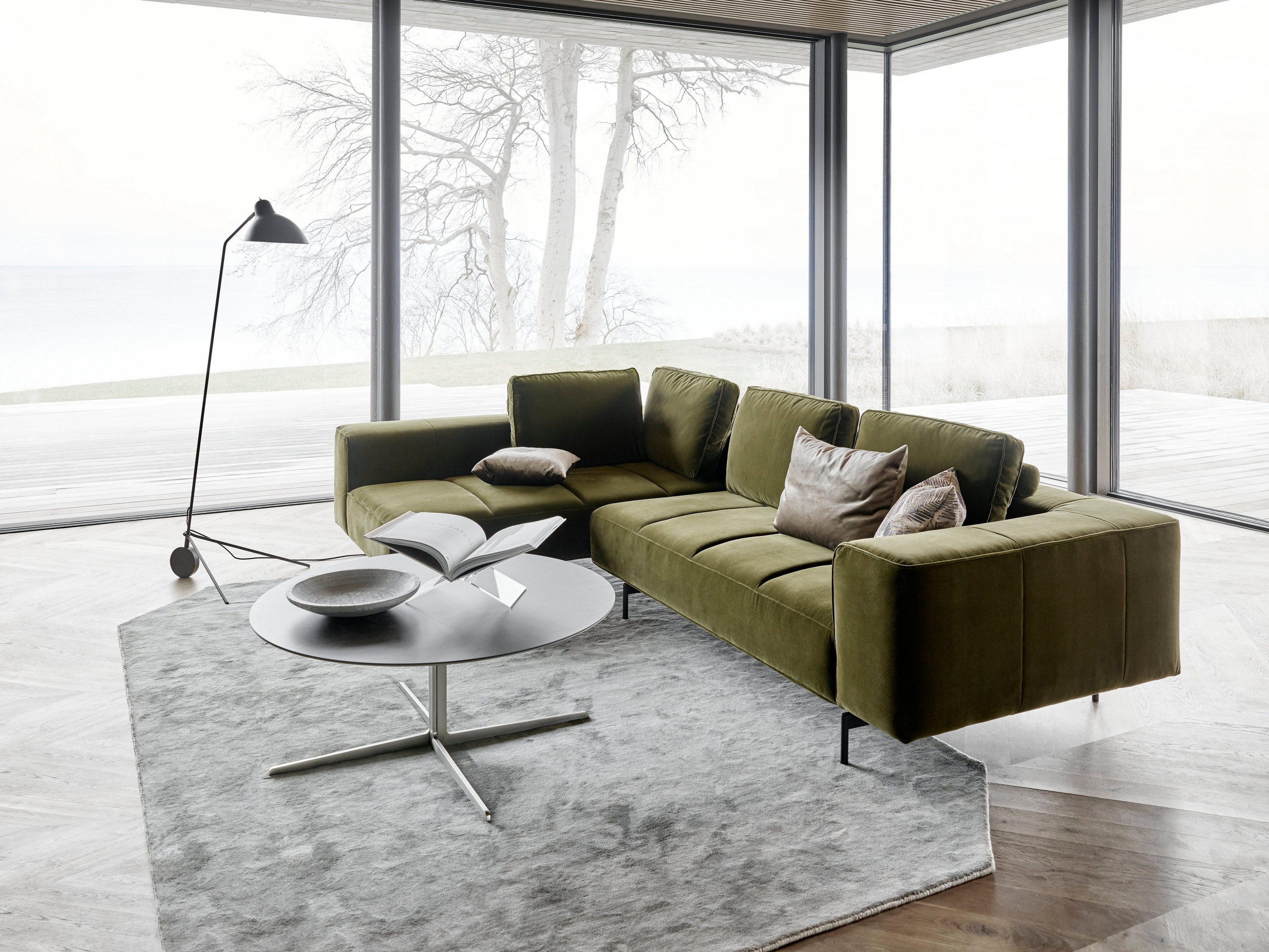 Modern green Amsterdam sofa, coffee table, floor lamp, by panoramic windows with a water view.