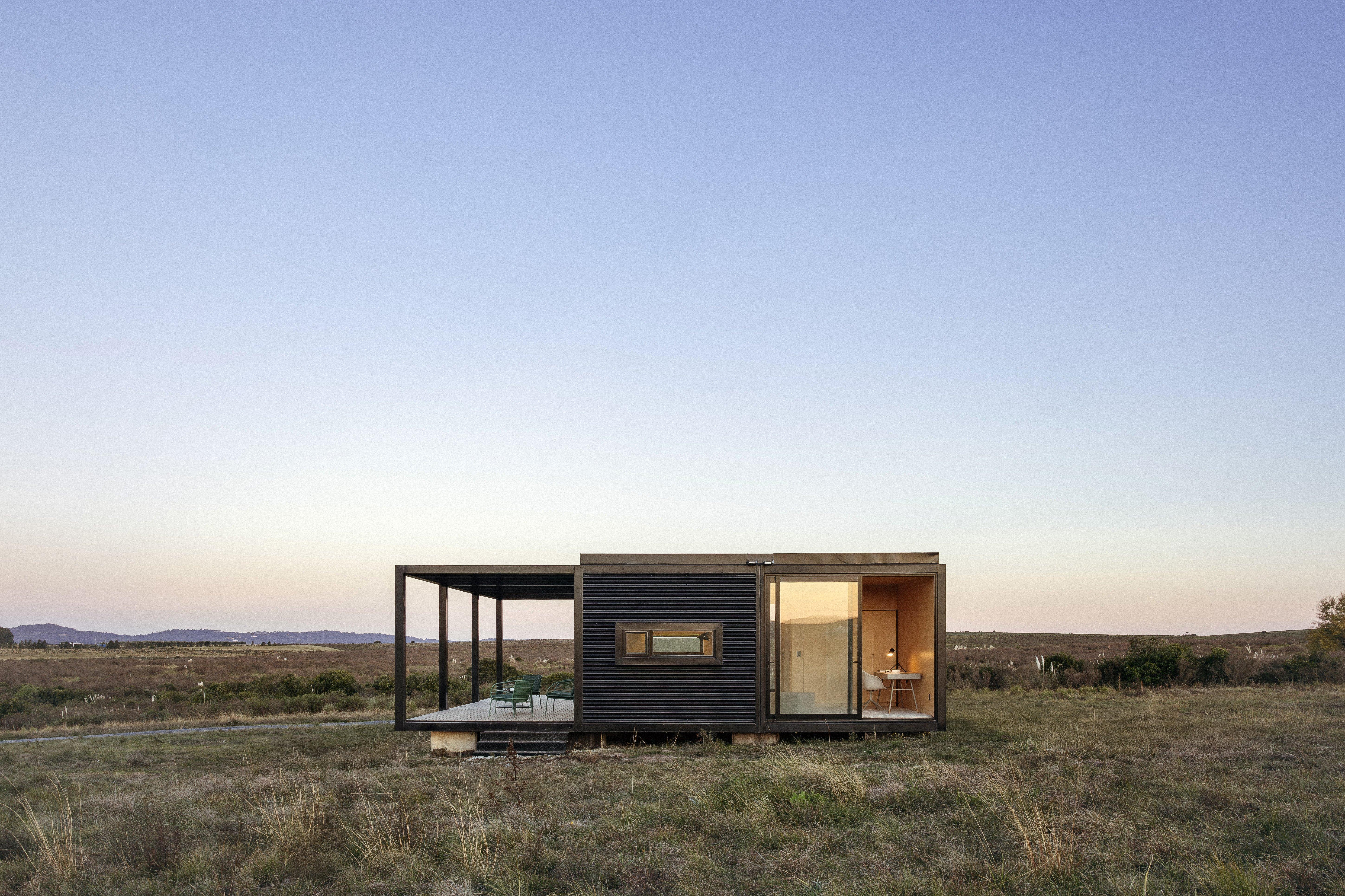 現代小屋，左側有露台和椅子，右側有玻璃窗和桌子。