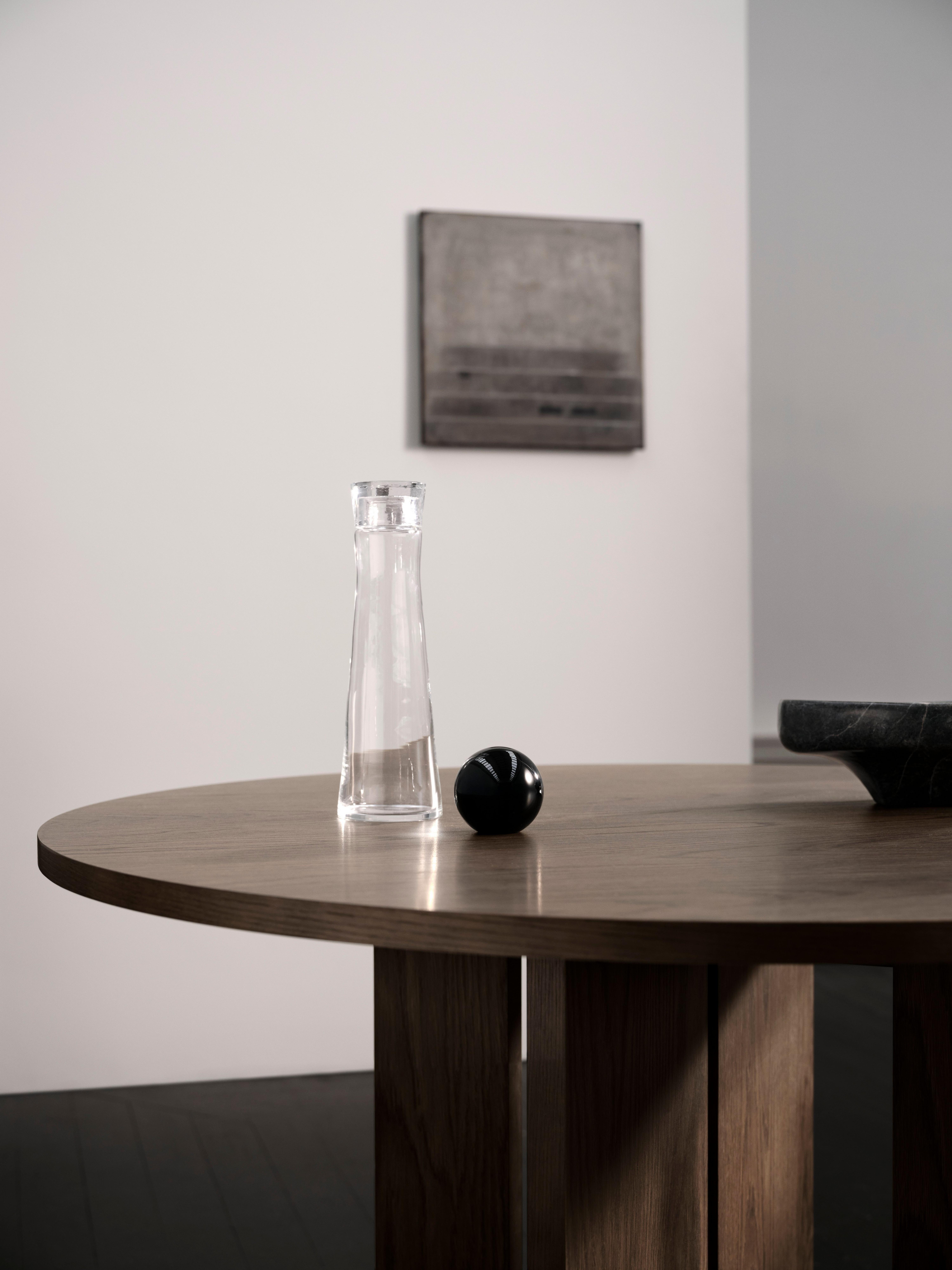 Glass carafe and black sphere on wooden table, with abstract art on the wall.