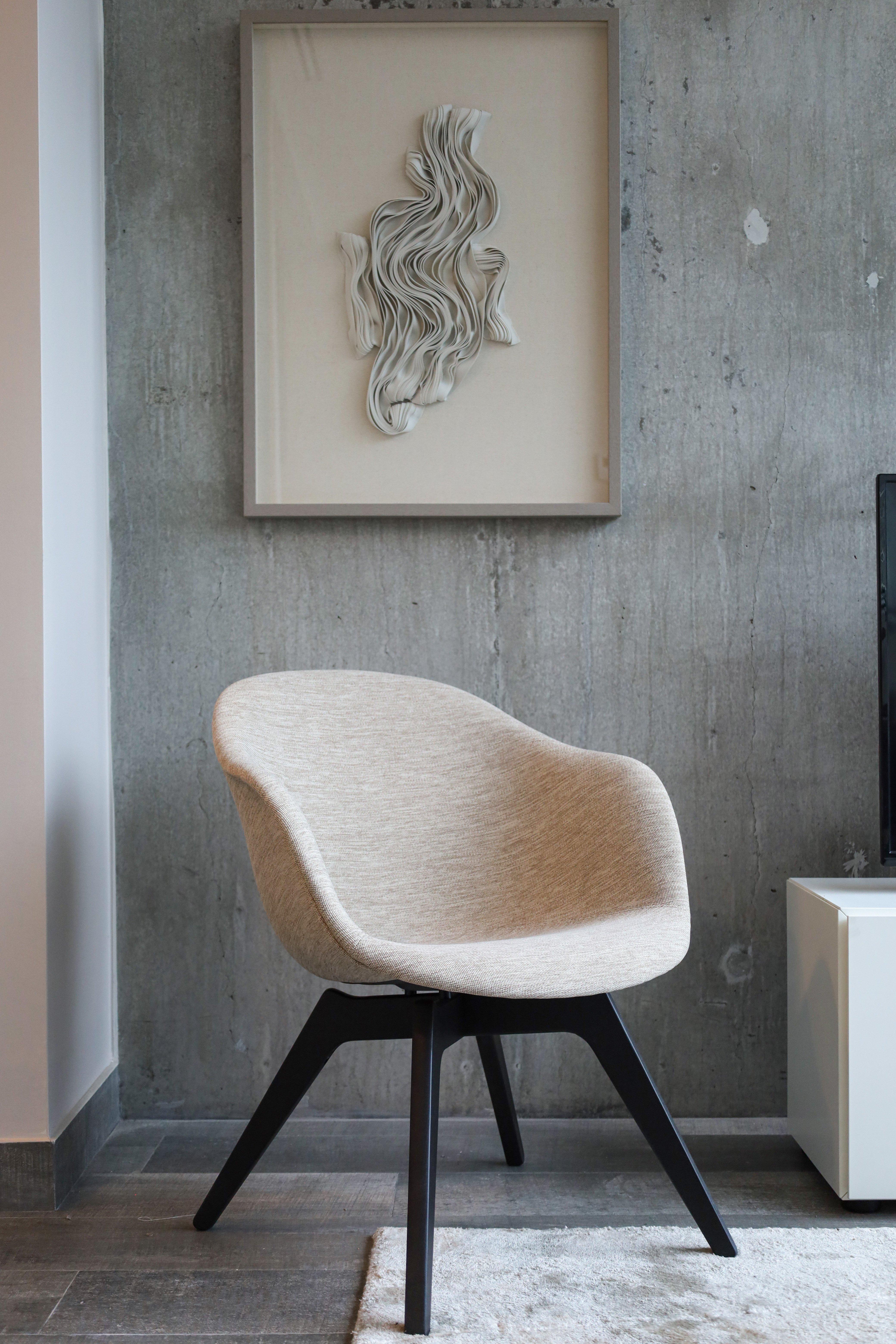 Beige chair with dark legs, abstract art on concrete wall above, beside a white cabinet.