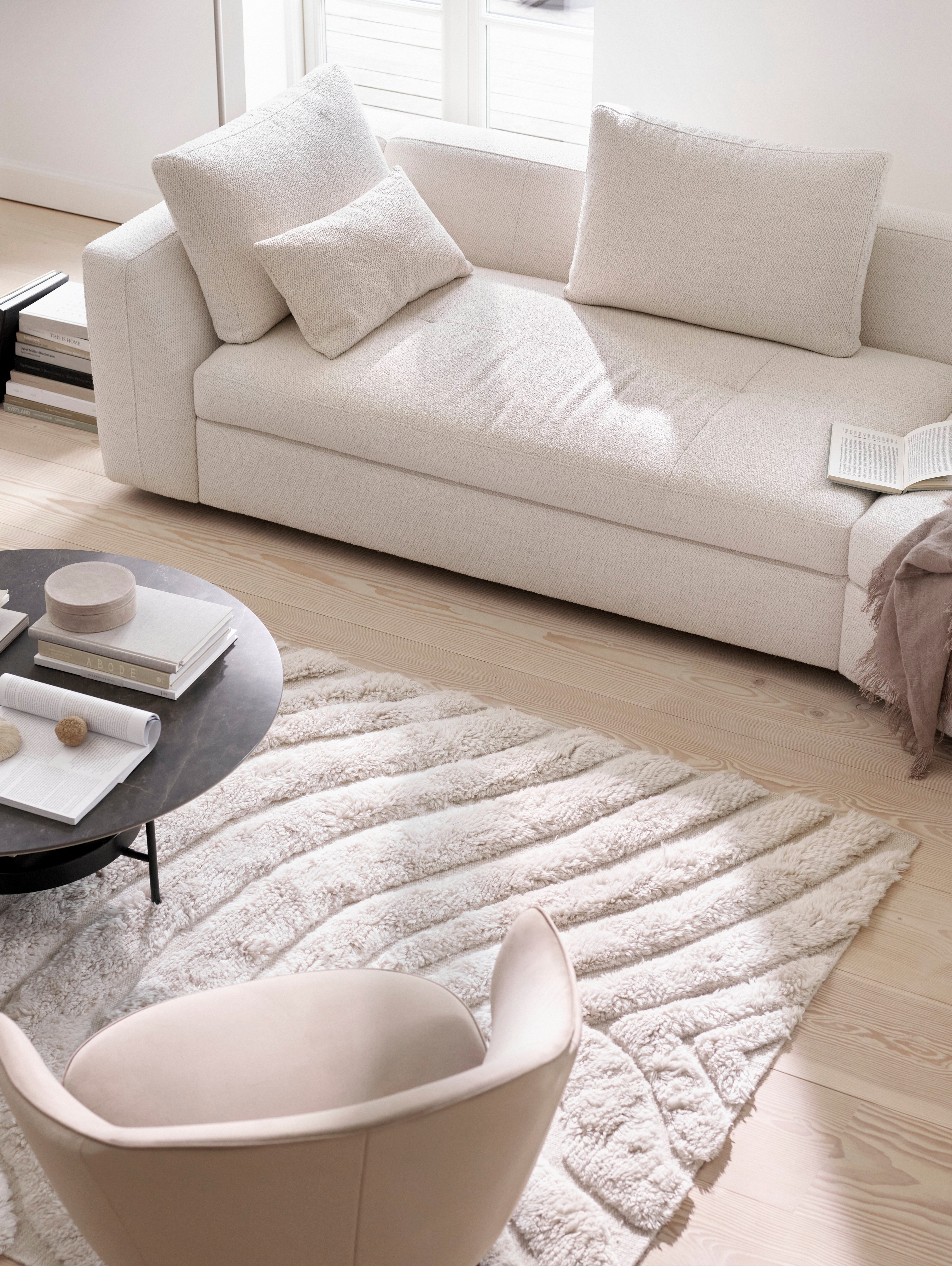 O sofá Bergamo com módulo relax redondo em tecido Lazio branco com a mesa de apoio Madrid com acabamento em revestimento de cerâmica em mármore escuro.